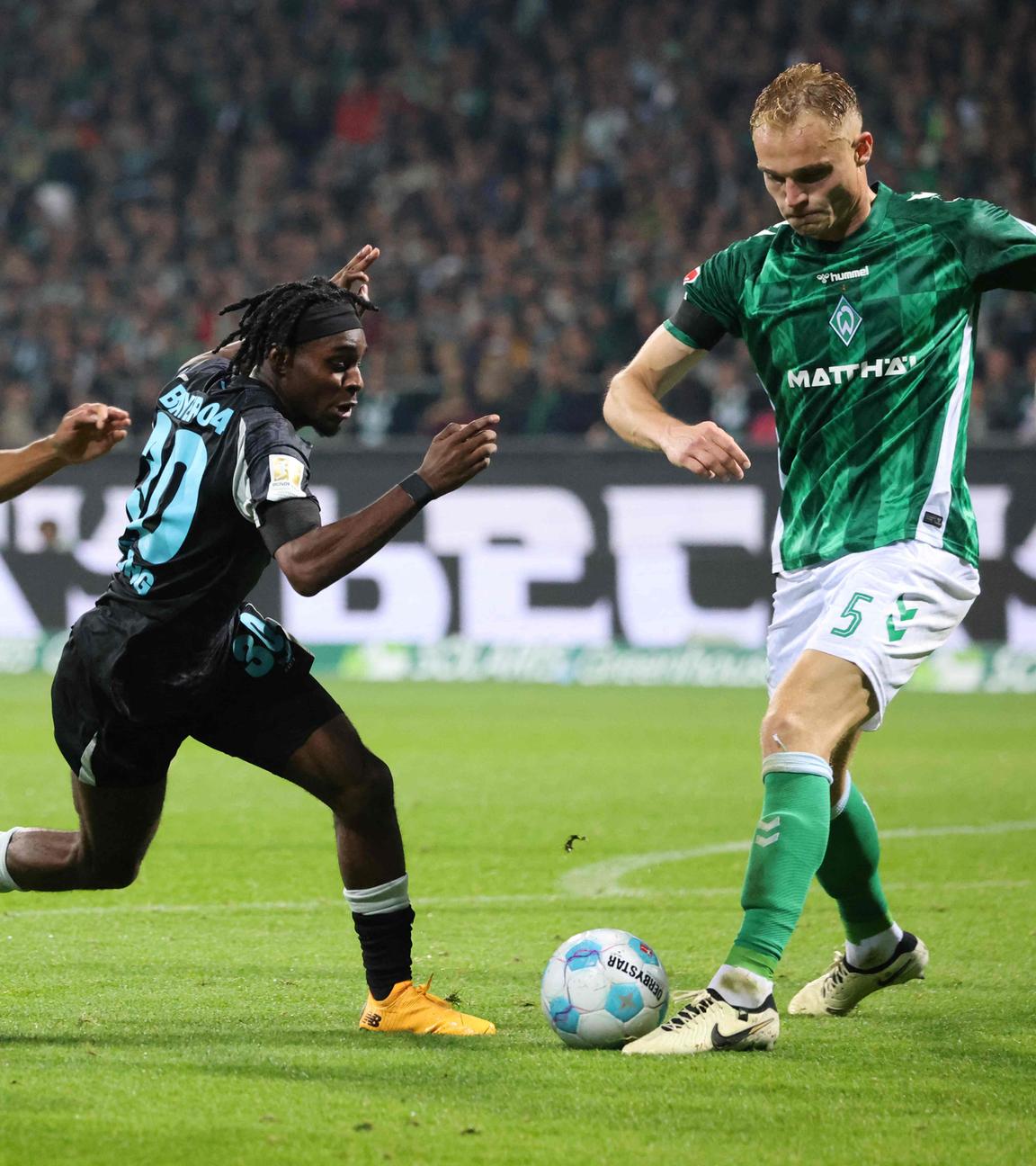 Bayer Leverkusens Verteidiger (Nr. 30) Jeremie Frimpong kämpft mit Bremens Stürmer (Nr. 07) Marvin Ducksch und Bremens Verteidiger (Nr. 05) Amos Pieper.