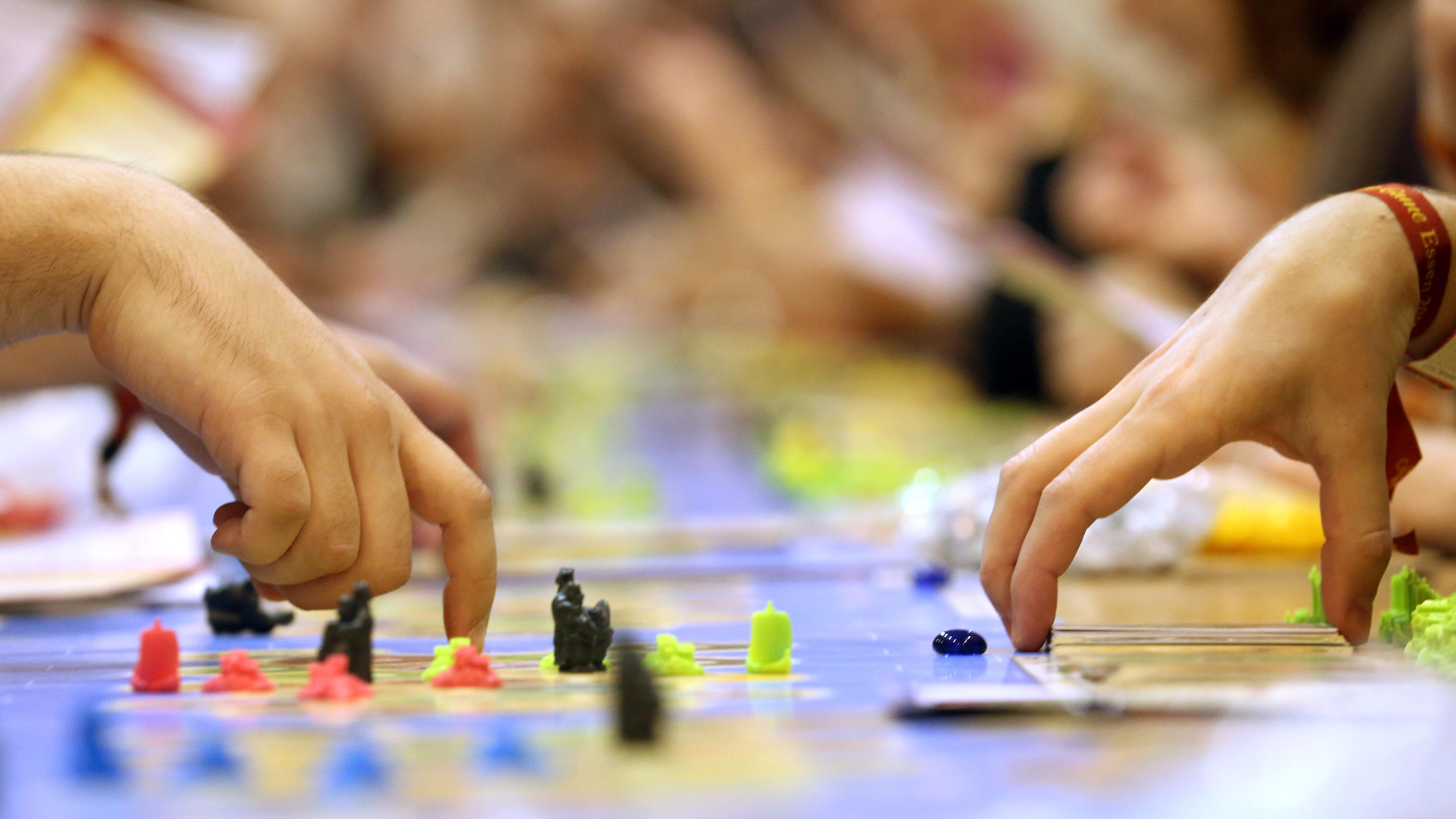 Zwei Hände bewegen die Spielfiguren auf einem Brettspiel.