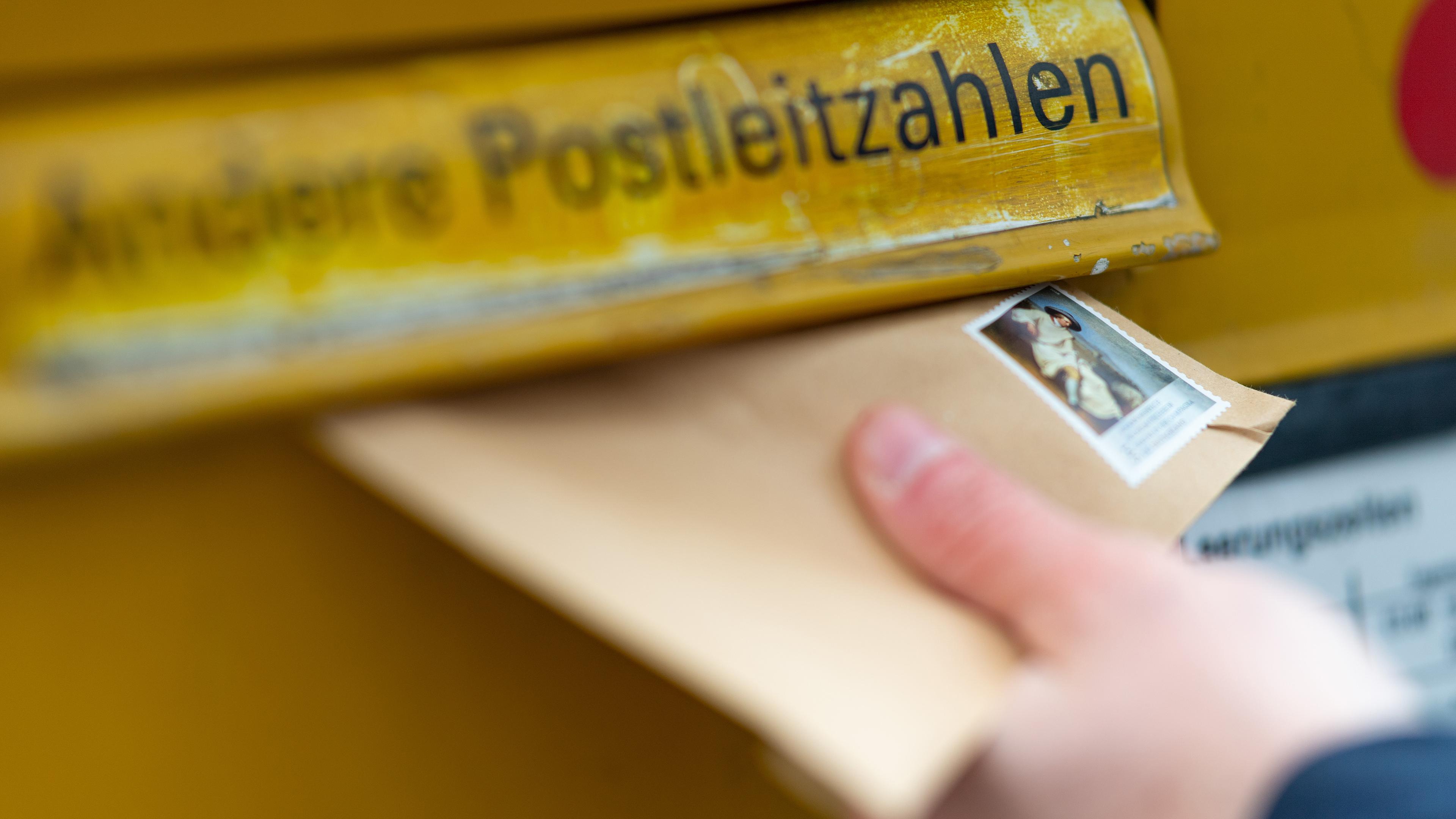 Person wirft einen Brief in einen Briefkasten