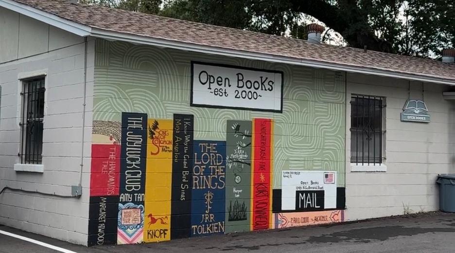 Außen an einer Hauswand sind mehrere Buchrücken aufgemalt, unter anderem von Herr der Ringe. Darüber steht der Name des buchladens "Open Books - est 2000".