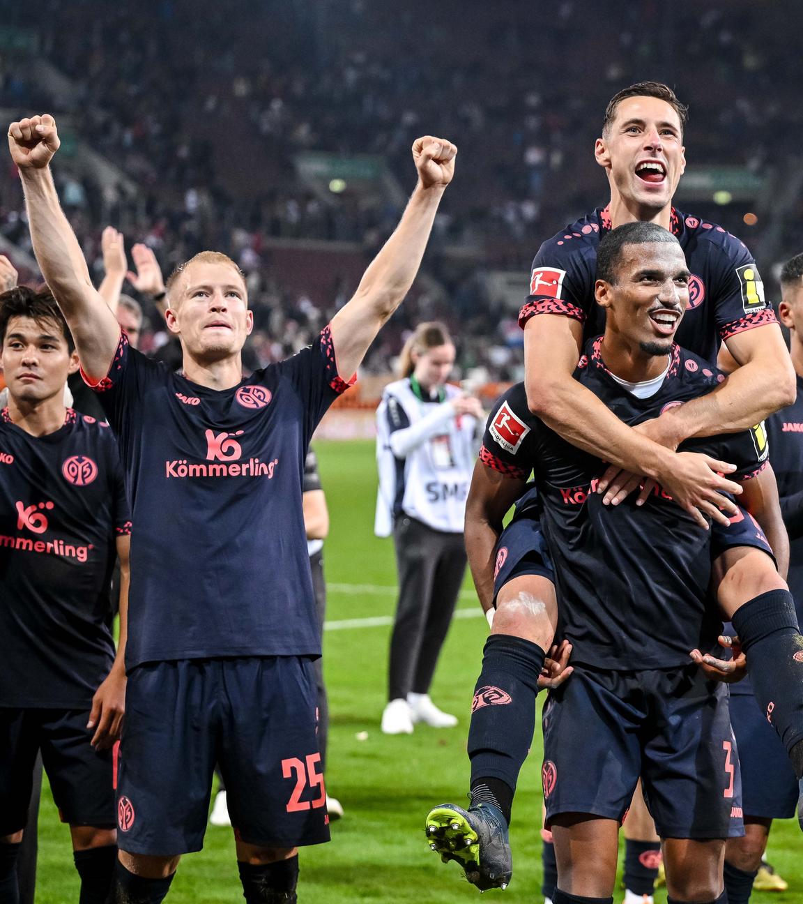 Die Mainzer Kaishu Sano, Andreas Hanche Olsen, Dominik Kohr, Mainzer Moritz Jenz und Mainzer Aymen Barkok feiern den Sieg gegen den FC Augsburg mit den Fans.