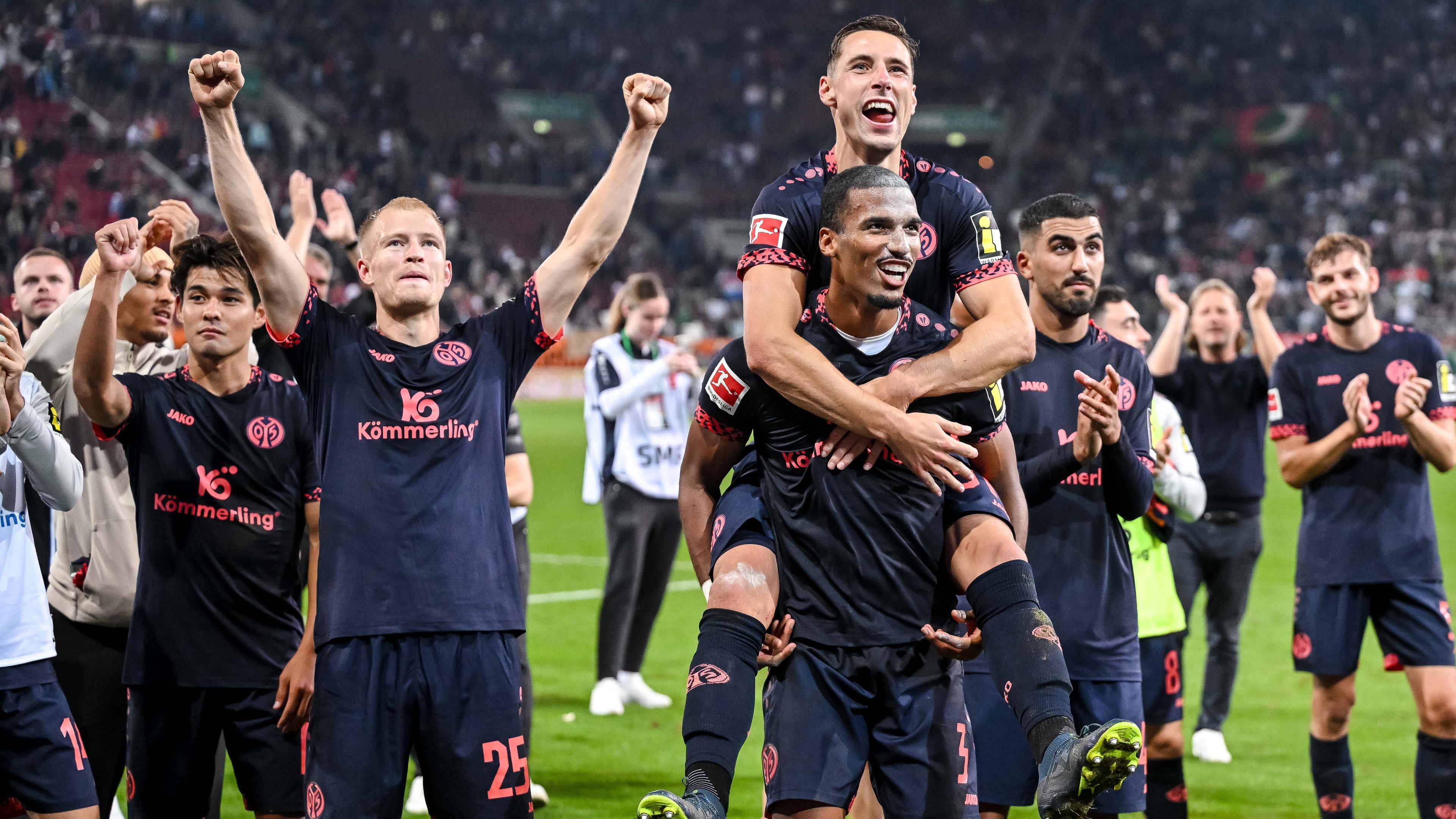 Die Mainzer Kaishu Sano, Andreas Hanche Olsen, Dominik Kohr, Mainzer Moritz Jenz und Mainzer Aymen Barkok feiern den Sieg gegen den FC Augsburg mit den Fans.