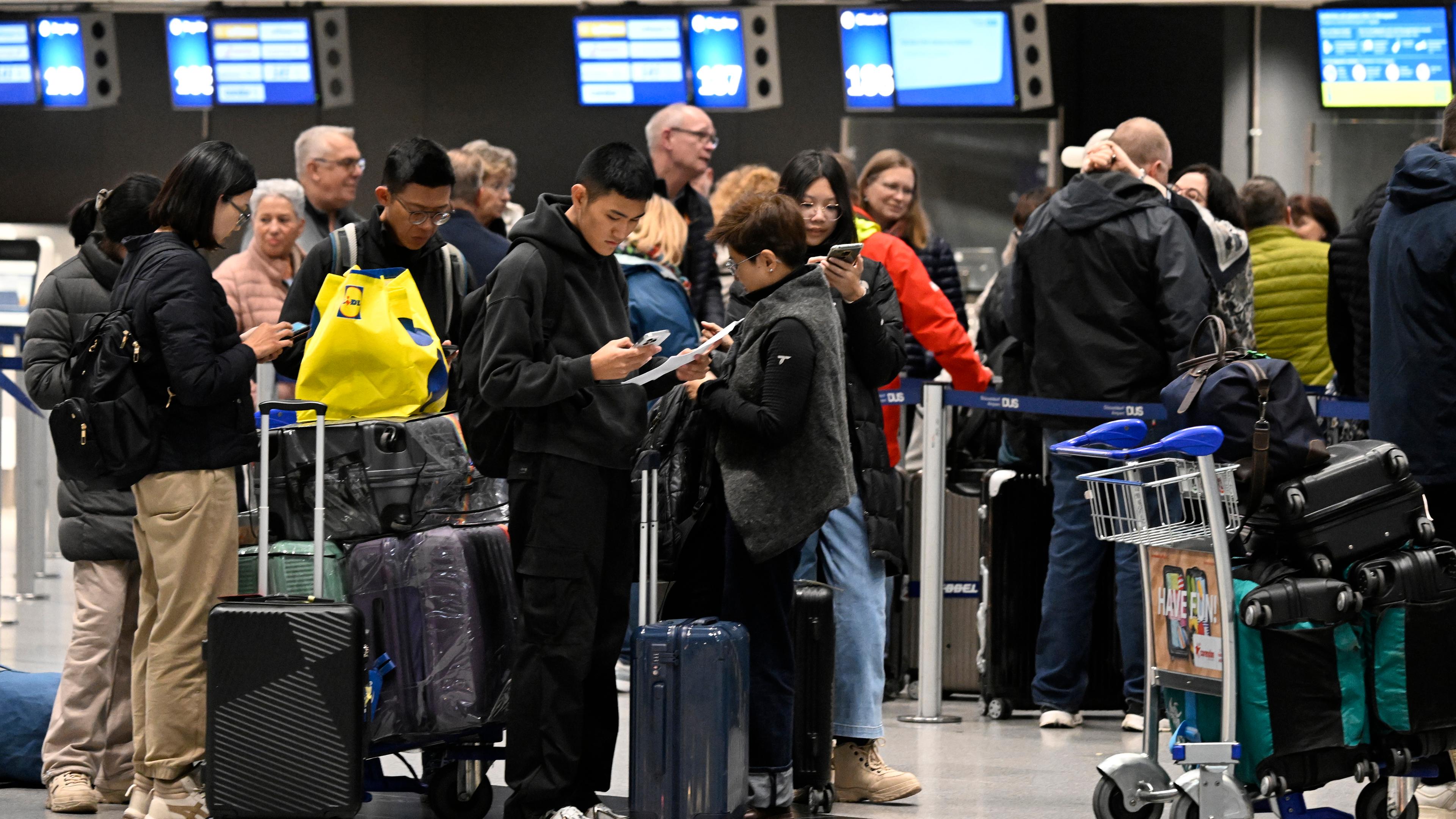  Reisende bilden am Flughafen beim Check-In eine Schlange.