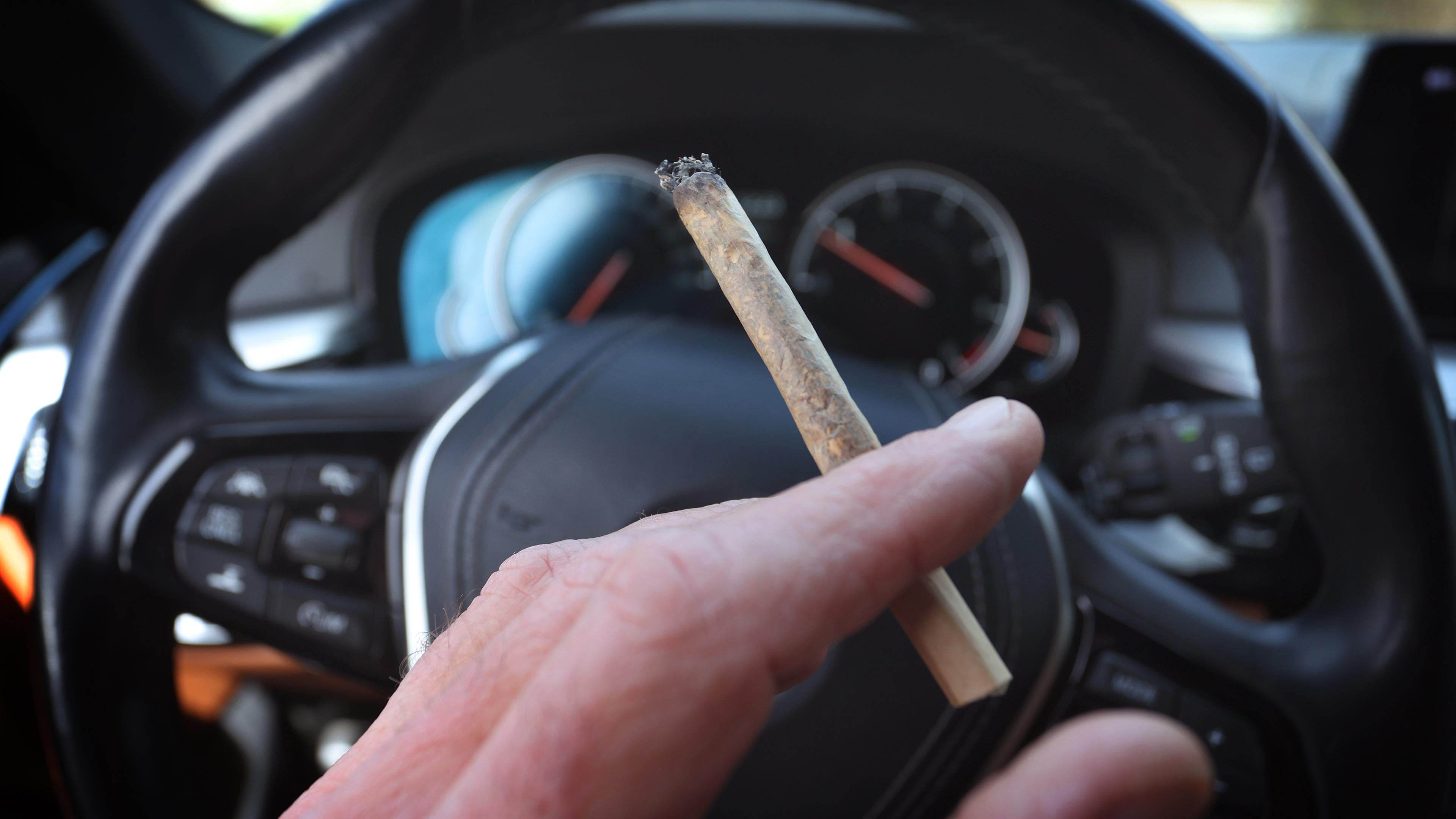Bayern, Kaufbeuren: Ein Mann sitzt mit einem Joint zwischen den Fingern am Steuer eines Autos.