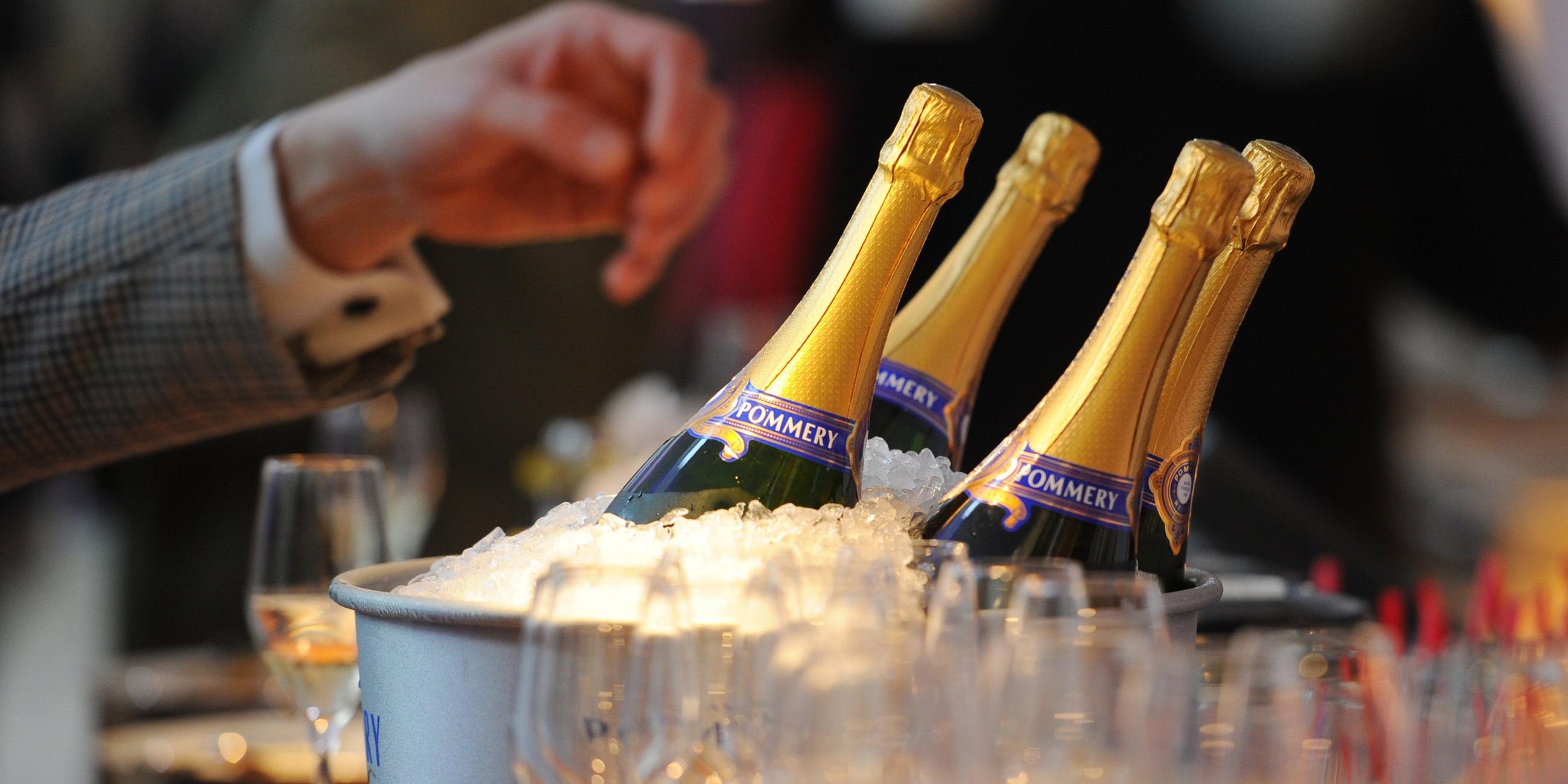 Vier Champagnerflaschen stehen auf einem Tisch in einem Champagnerkühler neben einigen Gläsern.