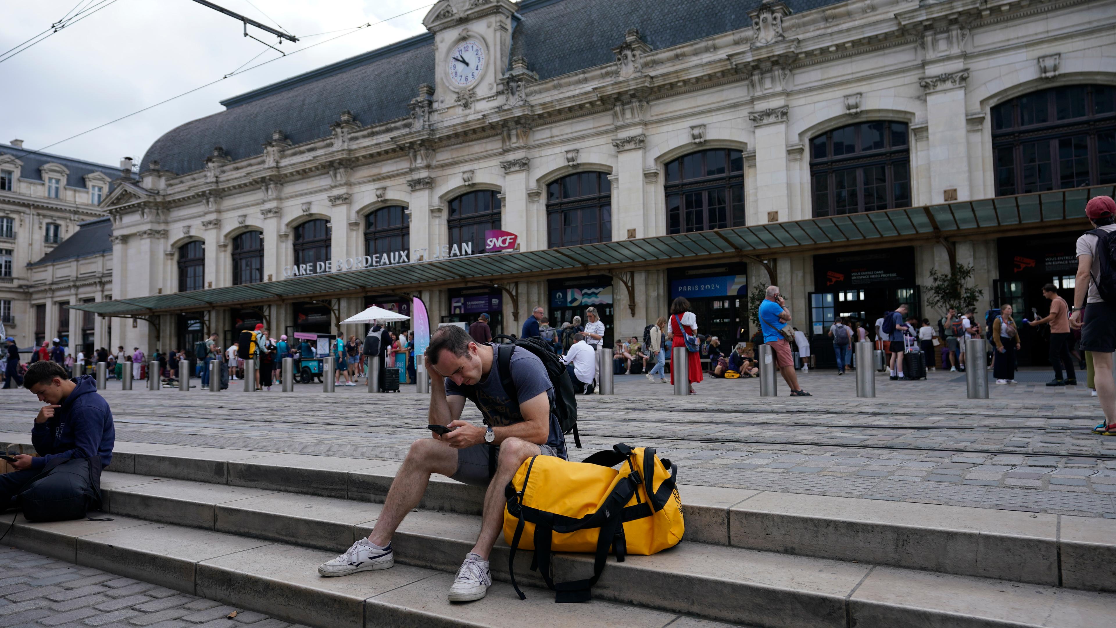 Ein Reisender sitzt auf den Stufen vor dem Bahnhof in Bordeaux und wartet.