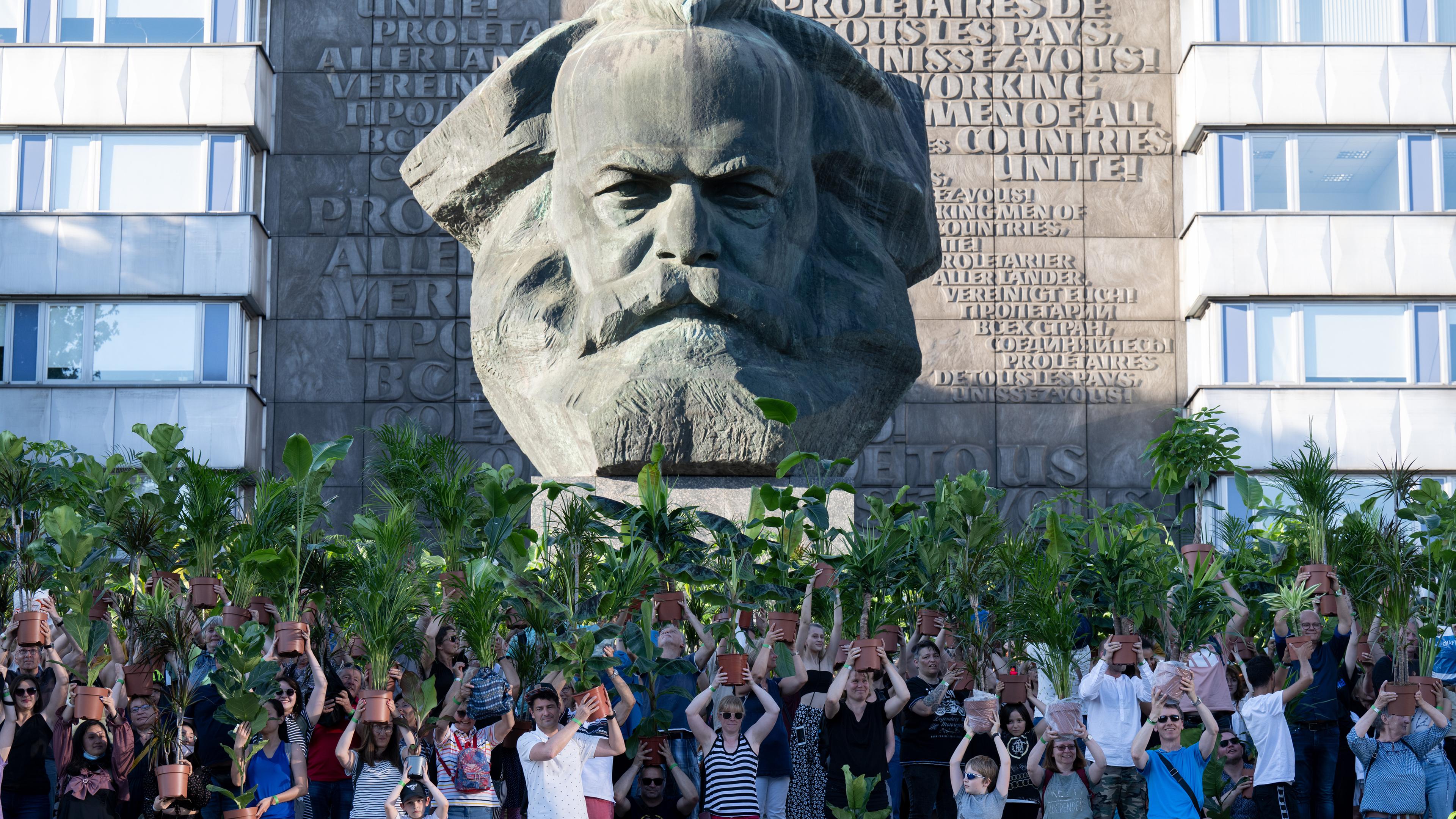 Sachsen, Chemnitz: Hunderte Teilnehmer einer Kunstperformance halten in der Innenstadt von Chemnitz ihre Zimmerpflanzen vor dem Karl-Marx-Monument, dem Wahrzeichen der Stadt, in die Höhe.