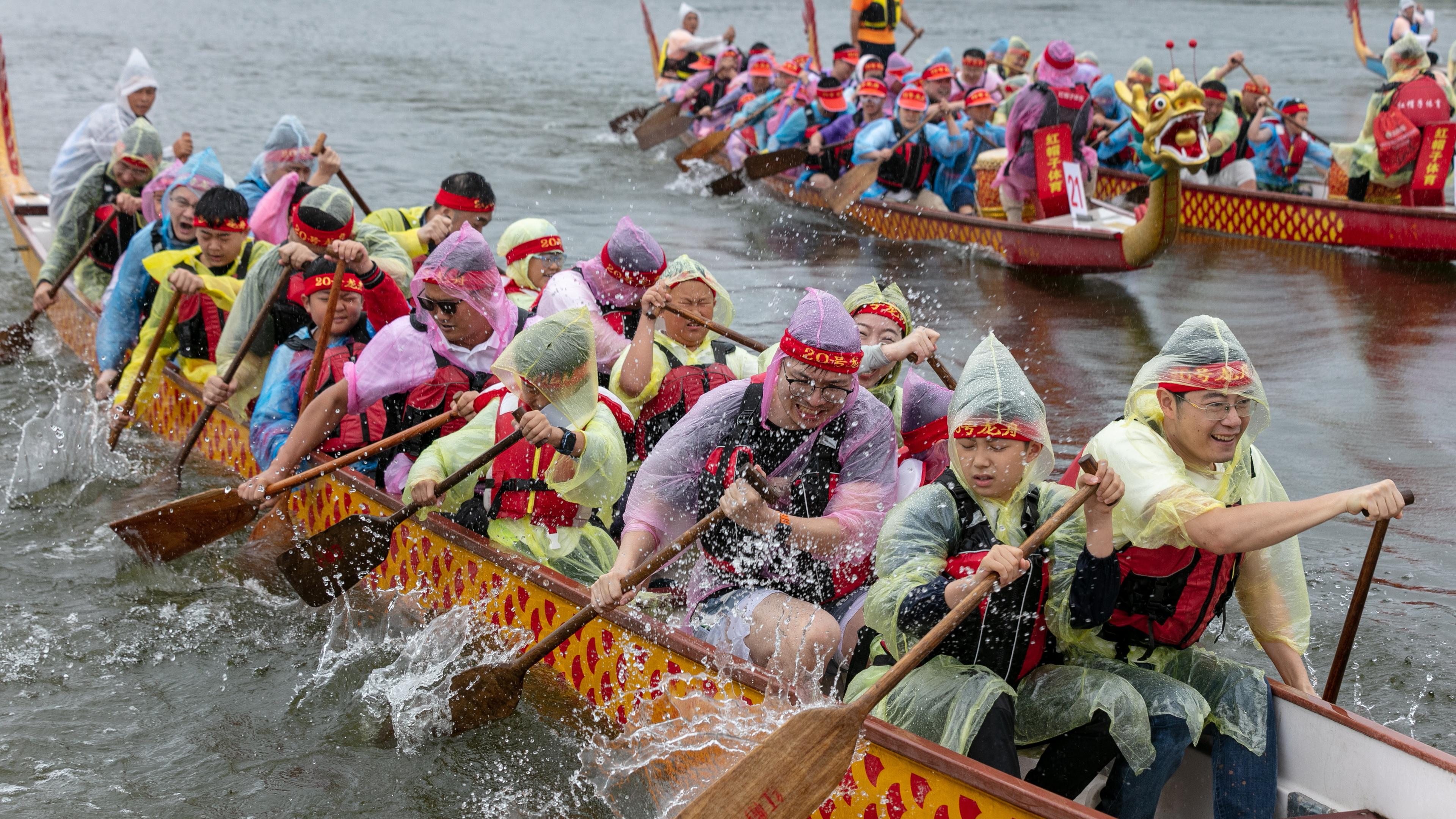 Menschen mit Regencapes auf einem Drachenboot in China.