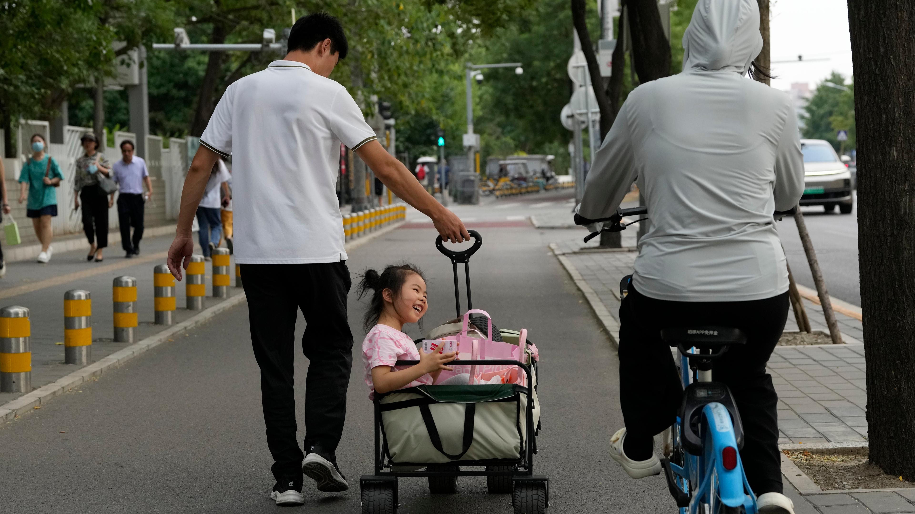 China: Ein Mann zieht ein Mädchen in einem Bollerwagen. 