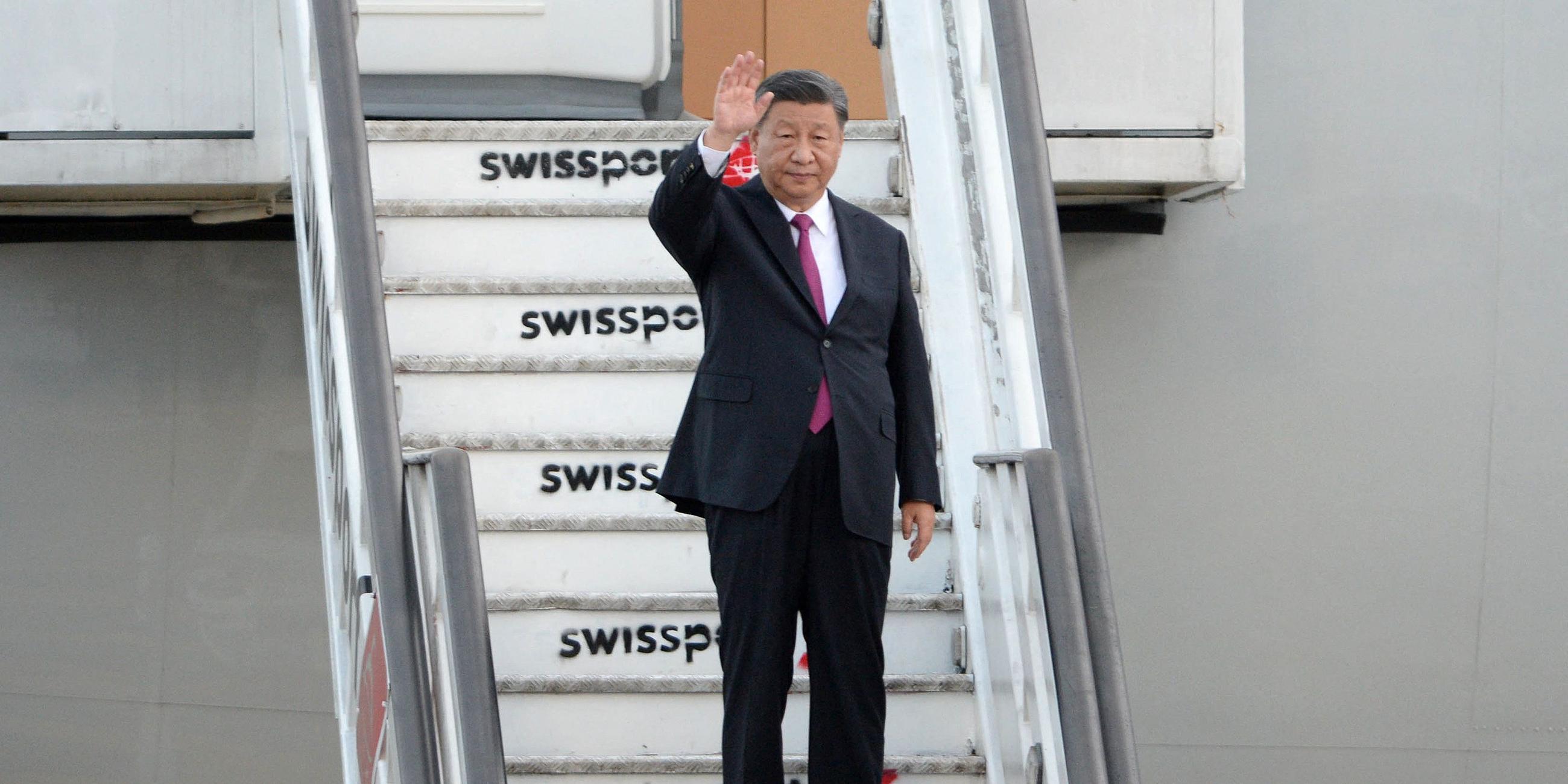 Chinas Staatsoberhaupt Xi Jinping steht auf den Treppen eines Flugzeugs und winkt.