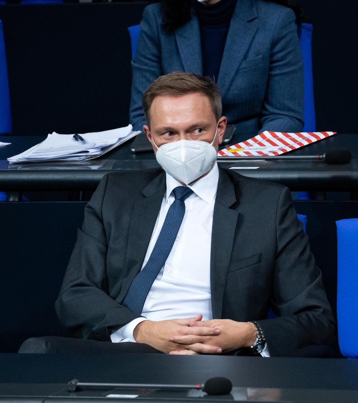 Christian Lindner sitzt im Bundestag auf einem Stuhl. Er trägt eine FFP2-Maske und schaut nach rechts. Er hat die Hände gefaltet.