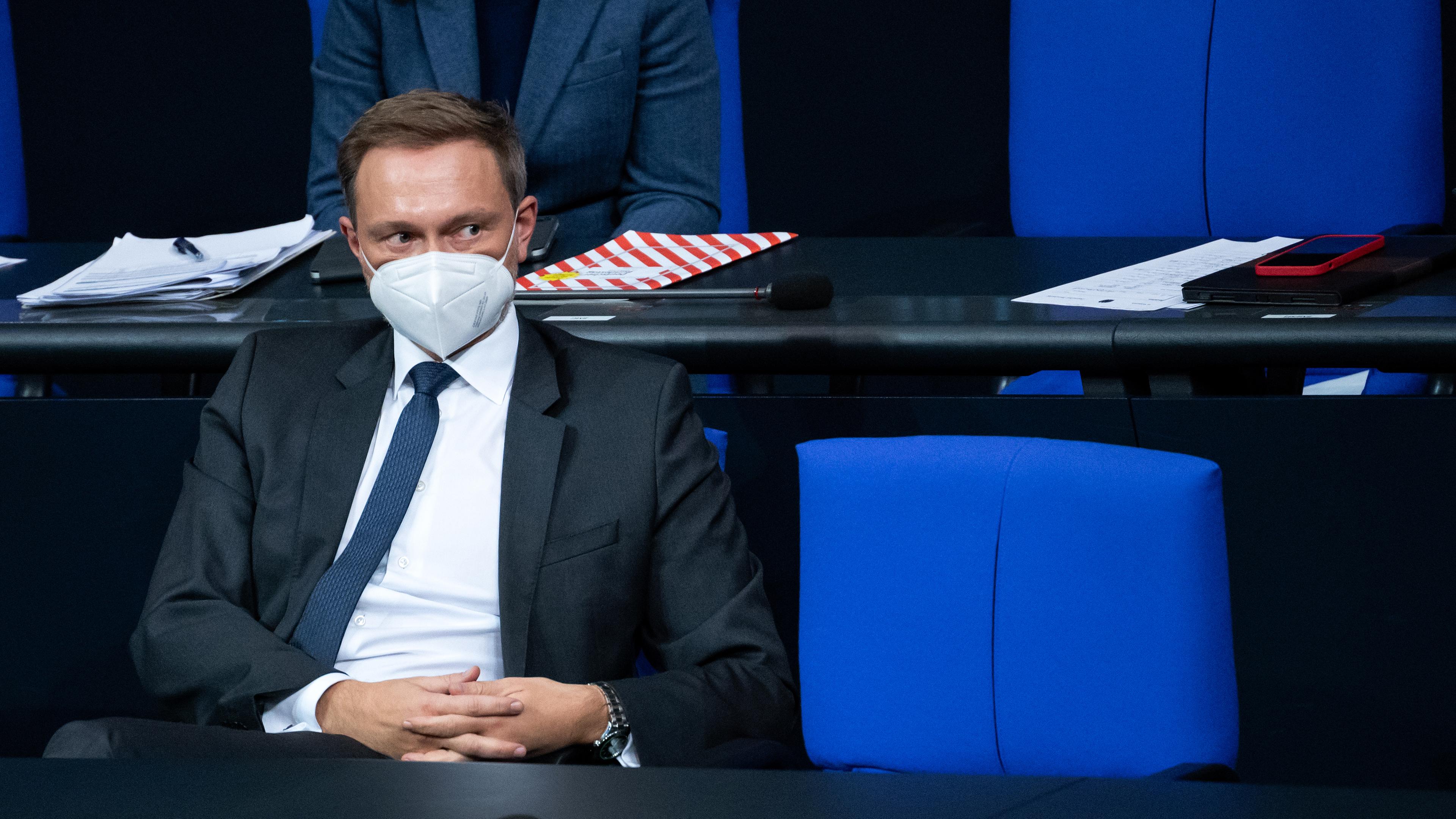 Christian Lindner sitzt im Bundestag auf einem Stuhl. Er trägt eine FFP2-Maske und schaut nach rechts. Er hat die Hände gefaltet.