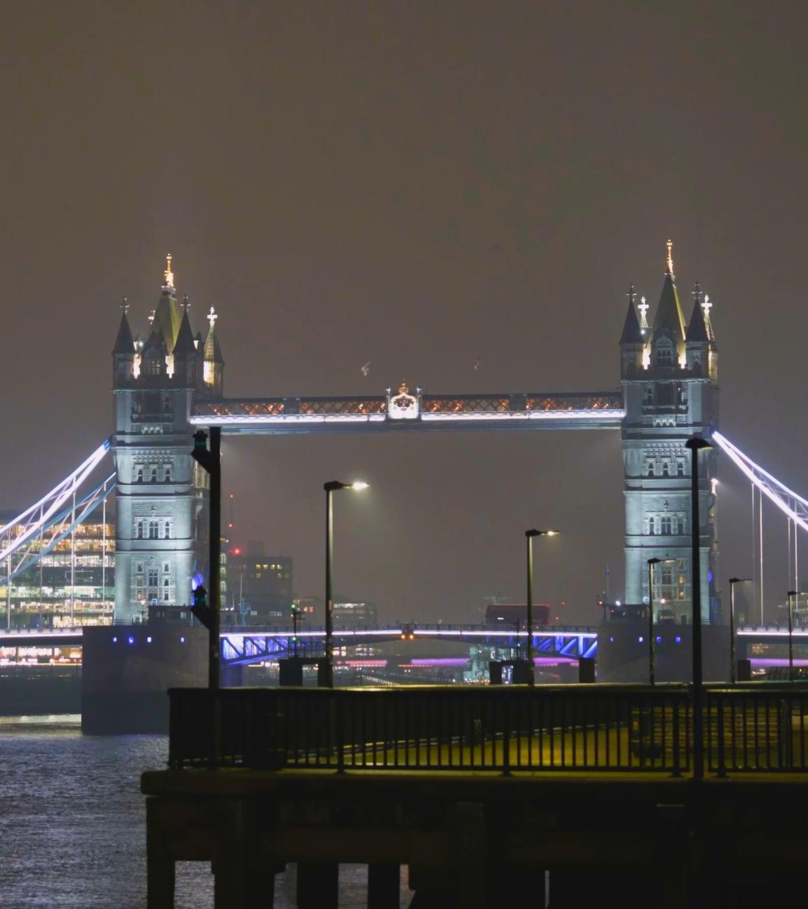 Blick auf London bei Nacht mit der beleuchteten Tower Bridge und mit Nebel im Hintergrund.