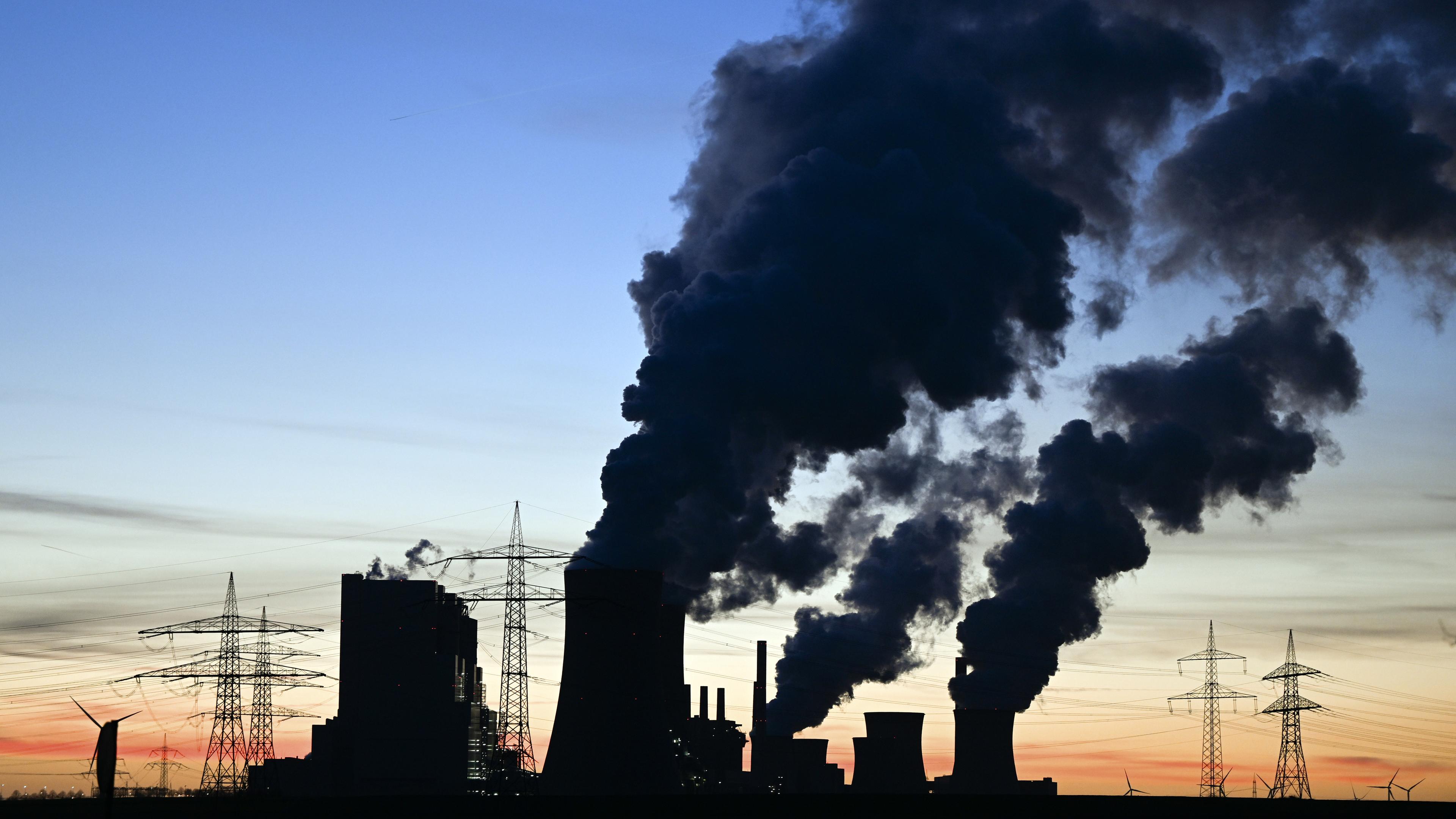 26.02.2022, Nordrhein-Westfalen, Rommerskirchen: Hinter dem Braunkohlekraftwerk Neurath ist die Sonne untergegangen und Rauch und Dampf steigen in den Abendhimmel.