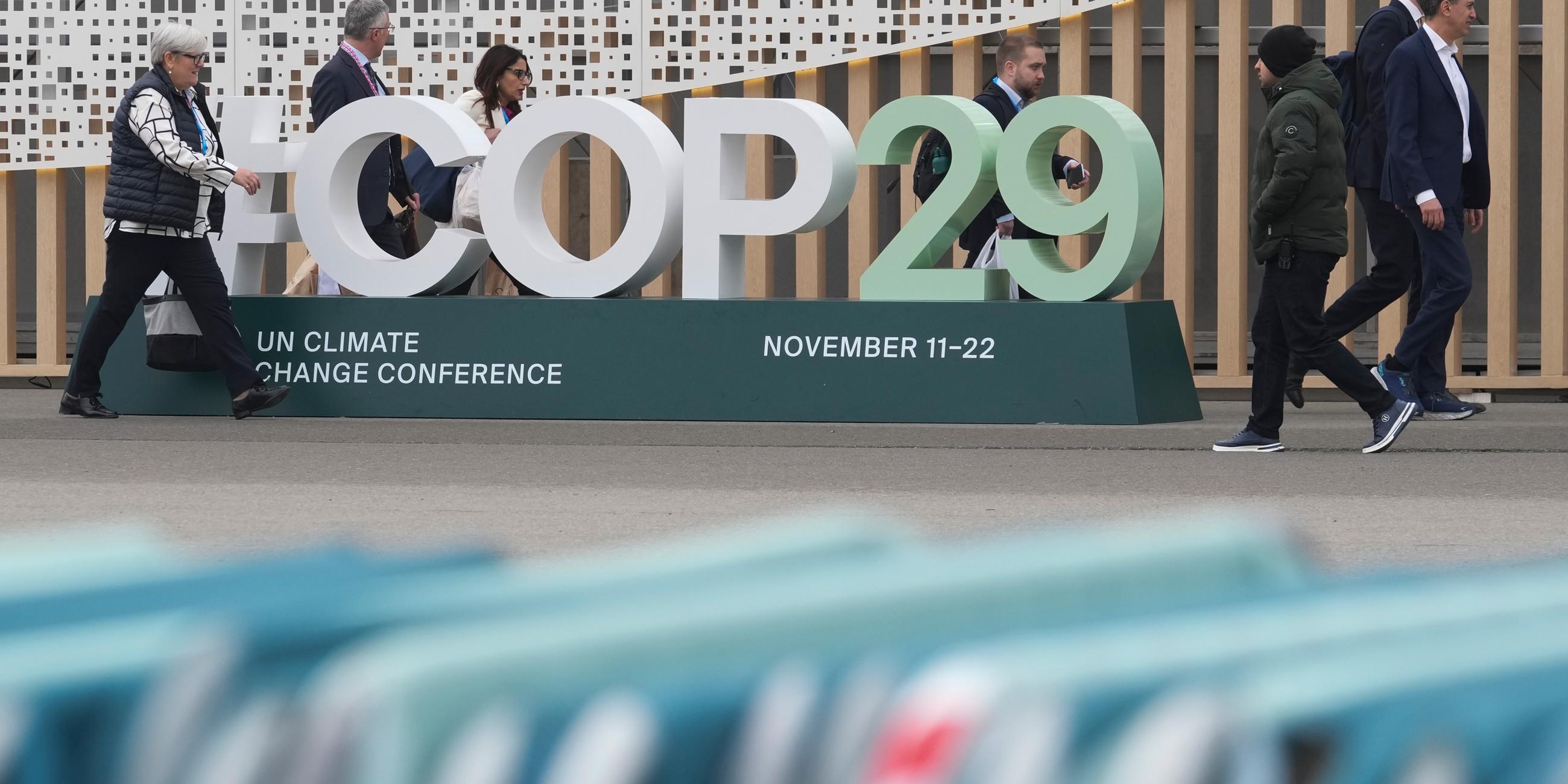 Teilnehmer gehen an einem Schild für den UN-Klimagipfel COP29 vor dem Veranstaltungsort vorbei-