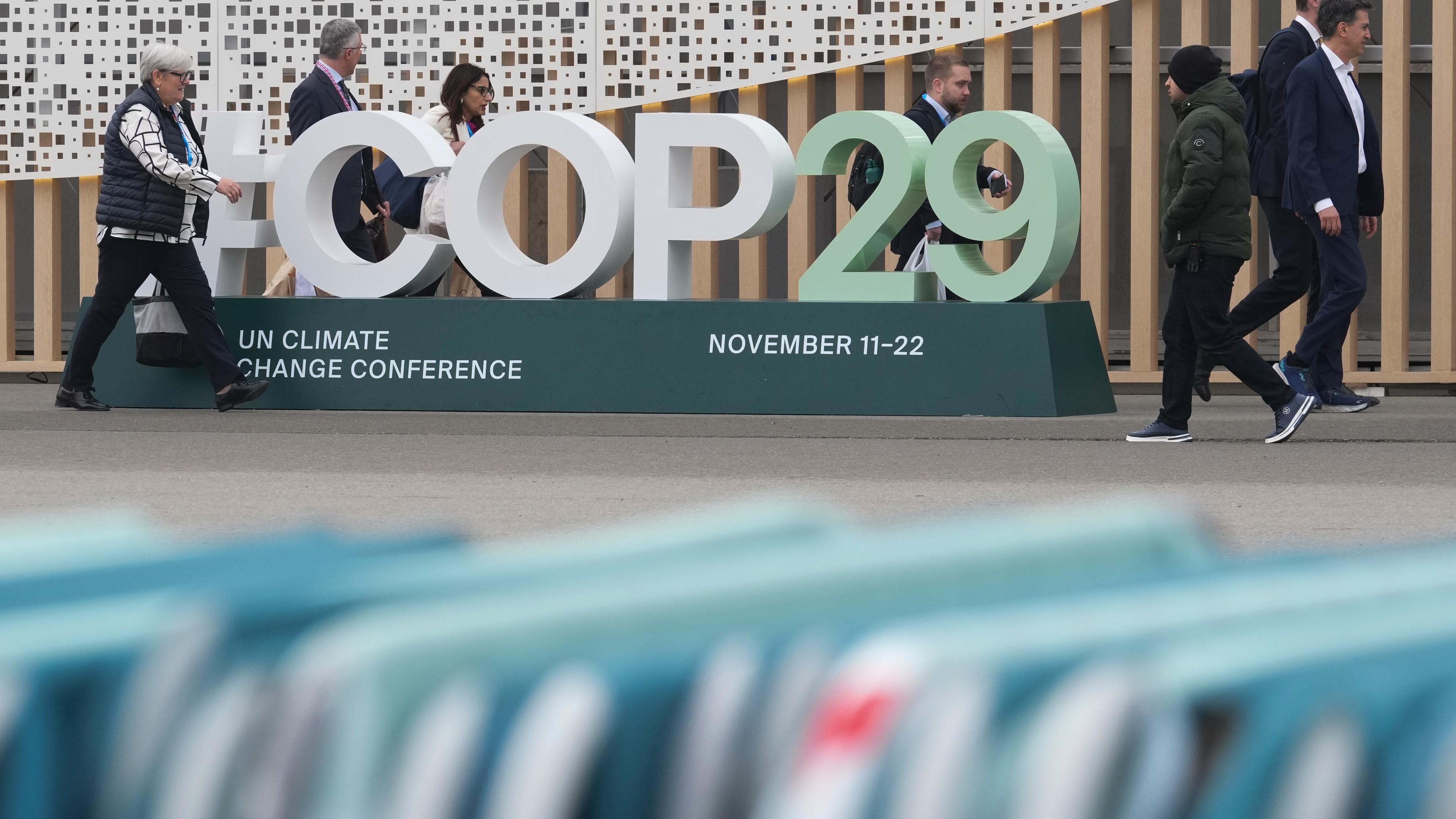 Teilnehmer gehen an einem Schild für den UN-Klimagipfel COP29 vor dem Veranstaltungsort vorbei-