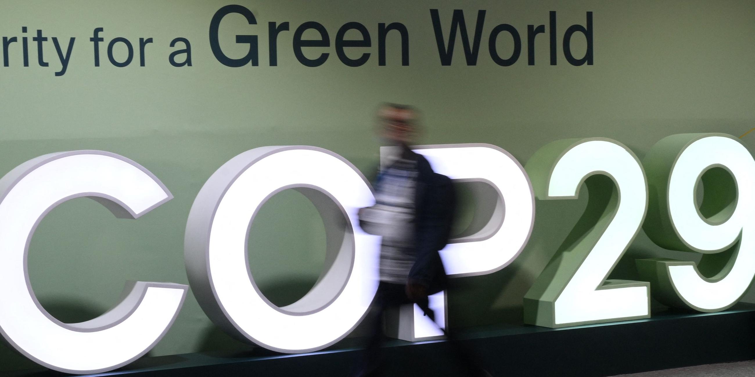 Teilnehmer laufen am COP29 Logo vorbei.