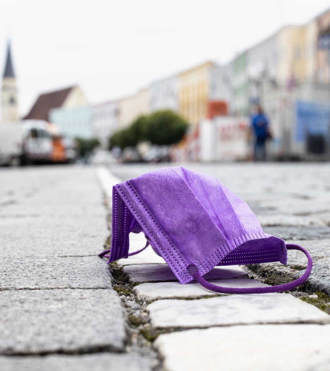 Eine lila OP-Maske liegt in einer Stadt auf Boden.