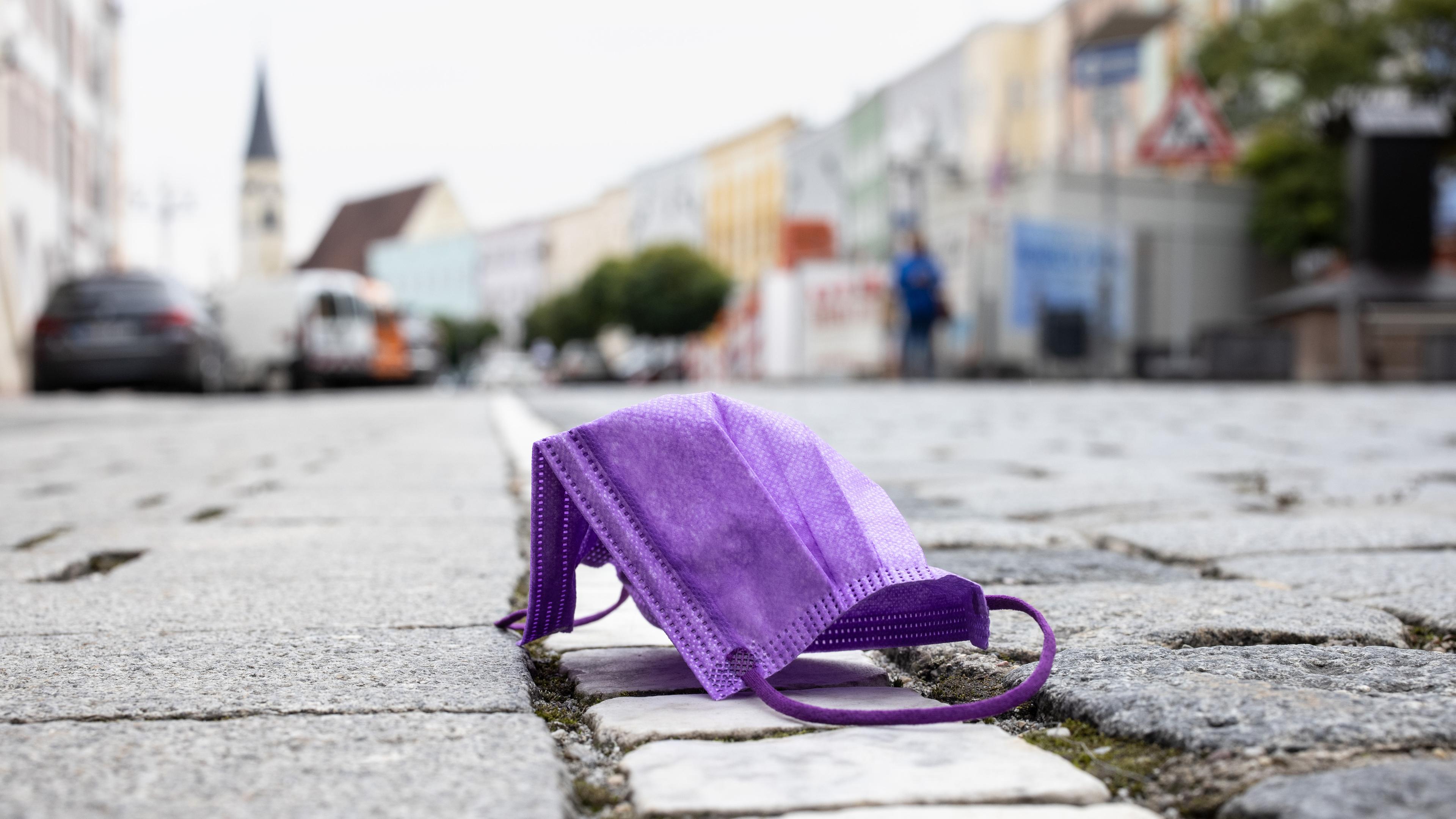 Eine lila OP-Maske liegt in einer Stadt auf Boden.