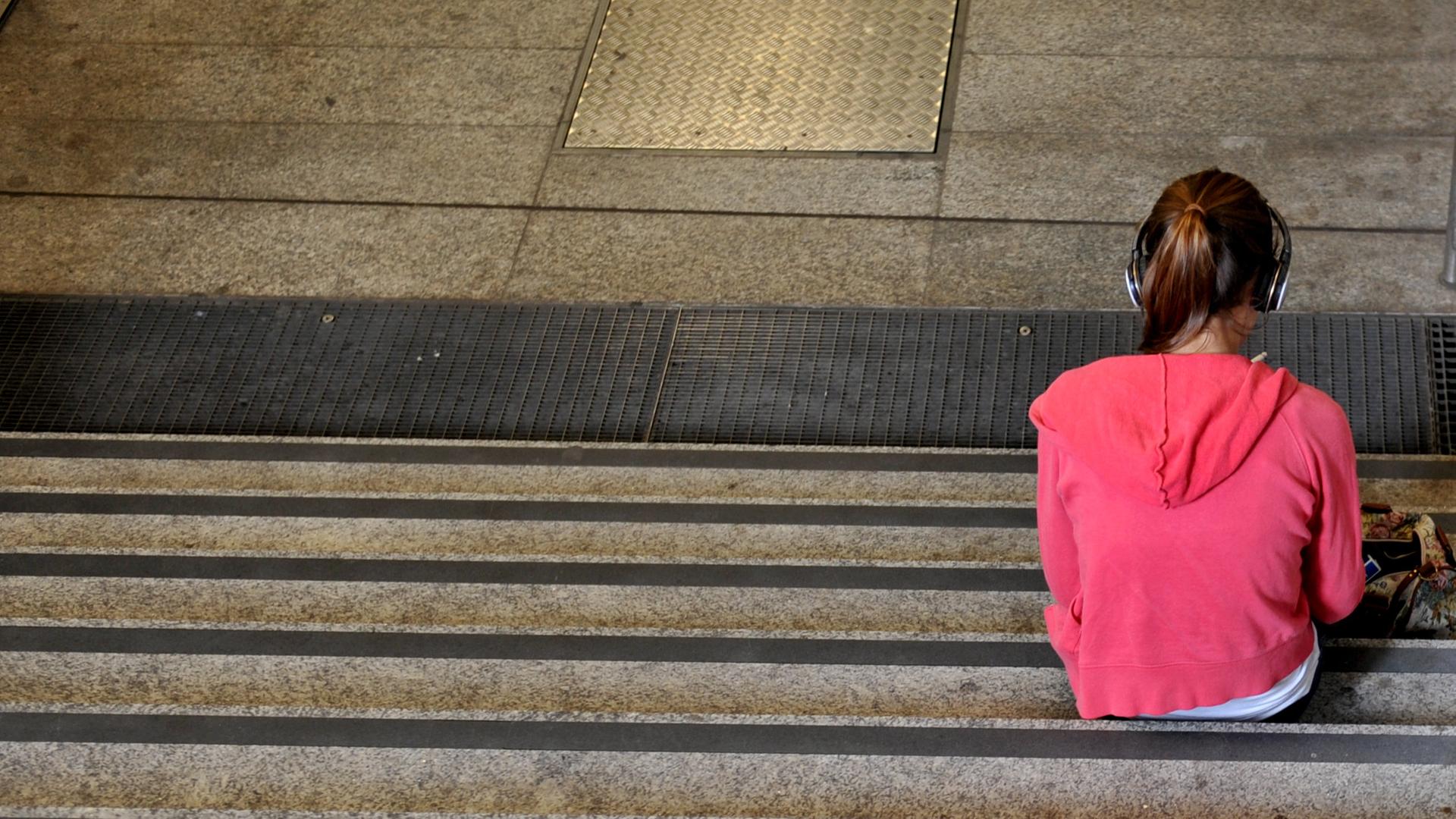 Ein Mädchen sitzt alleine auf der Treppe und hört Musik. 