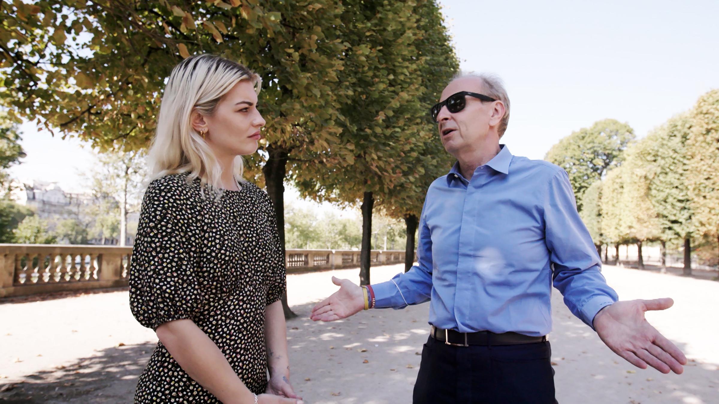 Yves Bouvier und Reporterin Sydney Lima stehen auf einer Allee in einem Park. Beide unterhalten sich, der Mann hält beide Handflächen nach oben.