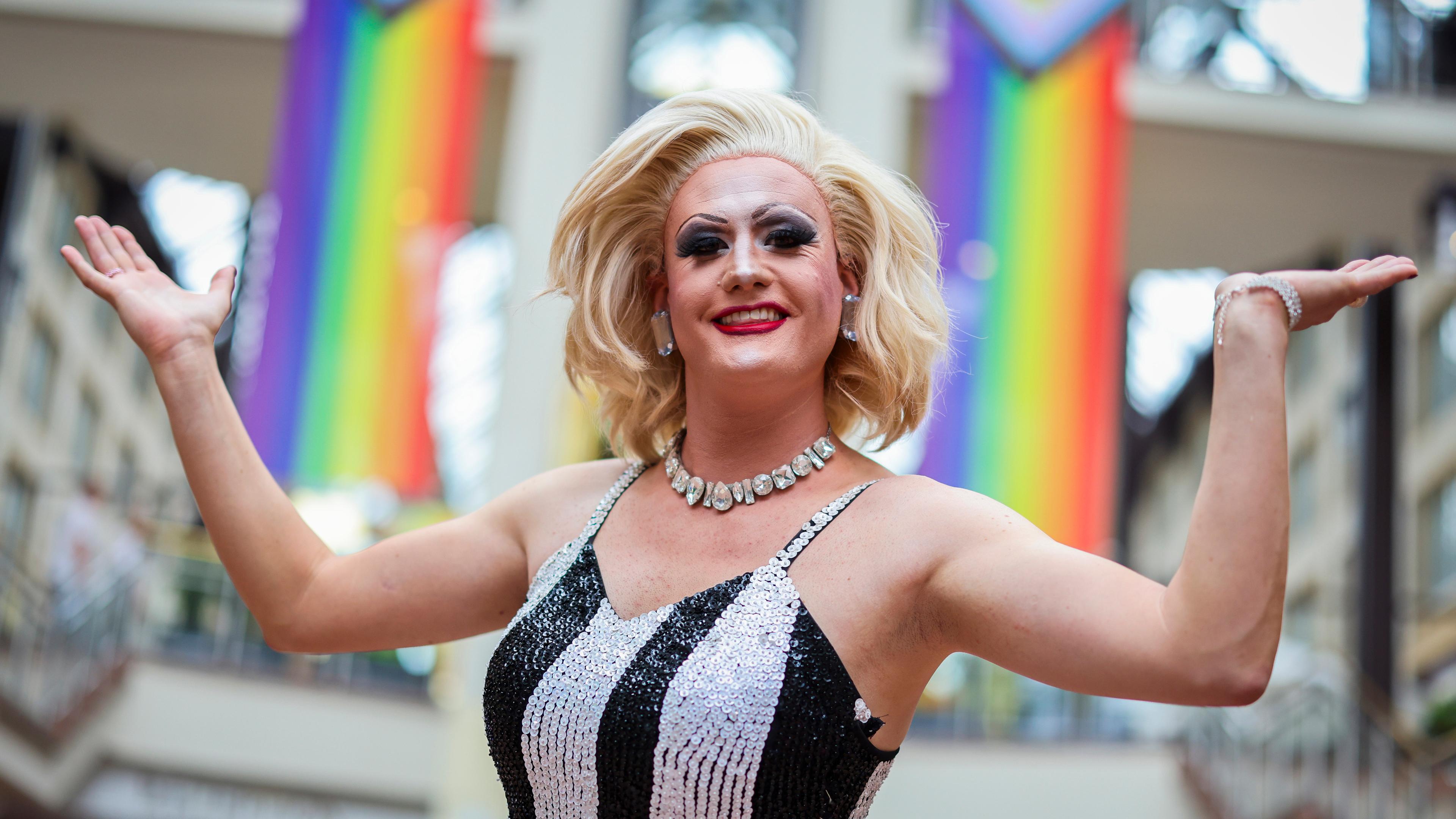 Dragqueen Meryl Deep steht vor zwei Pride Regenbogenfahnen vor dem ColognePride am 21.07.2024.