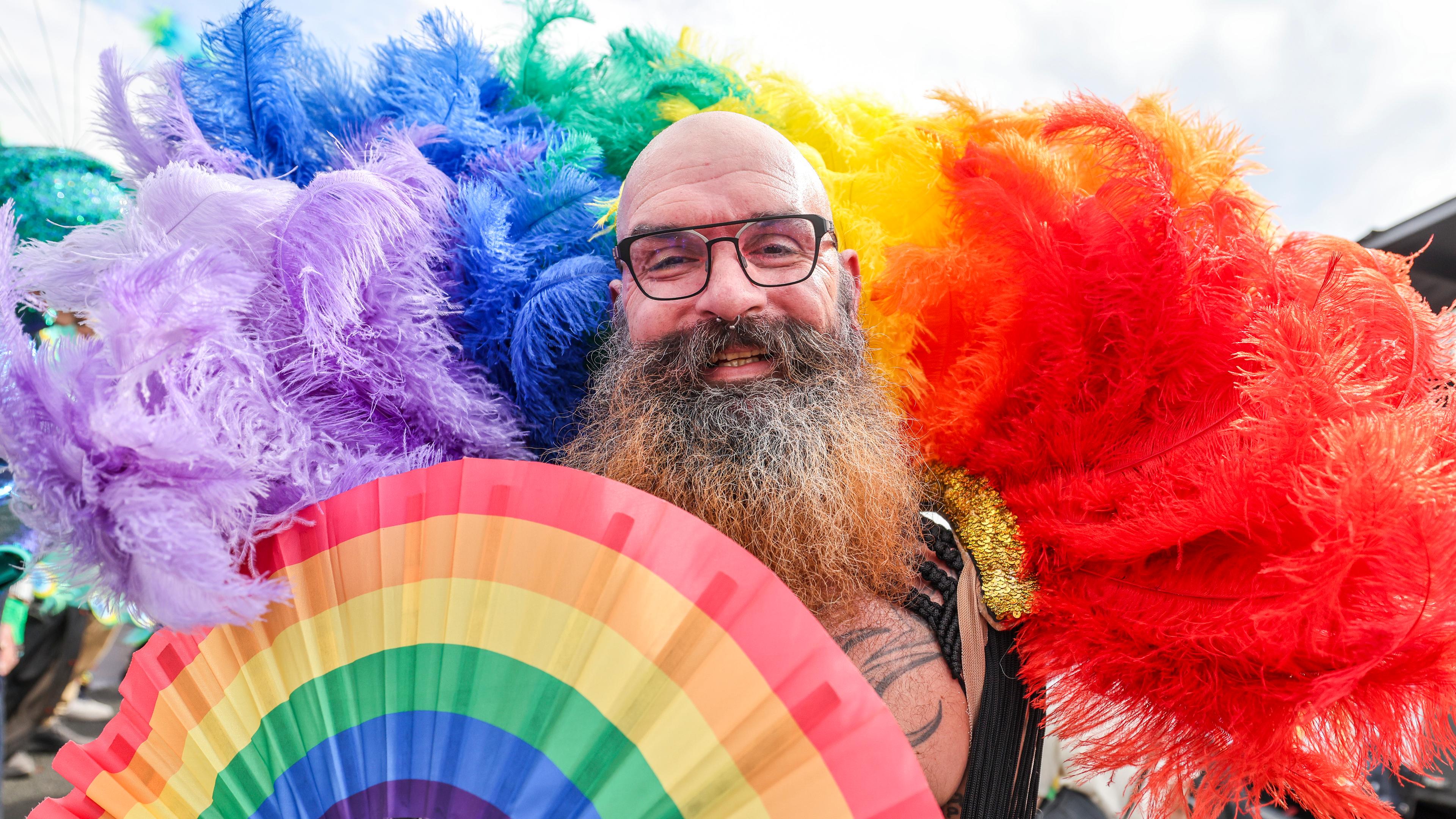 Ein Mann mit Regenbogenfächer und Federn in Regenbogenfarben beim Christopher Street Day in Köln.