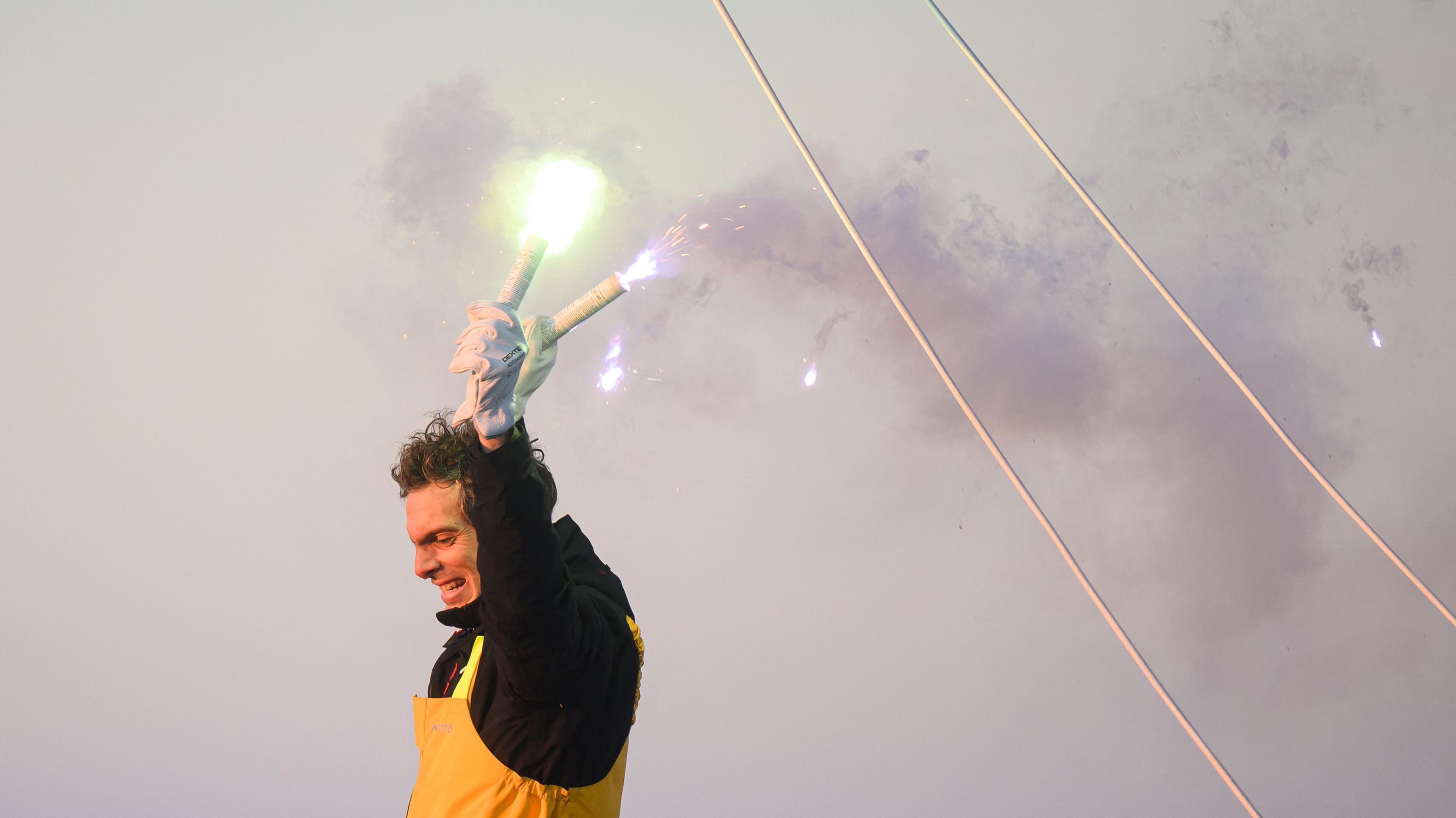 Vendee-Globe-Sieger Charlie Dalin hält im Ziel zwei Pyrotechnik-Fackeln in die Höhe.