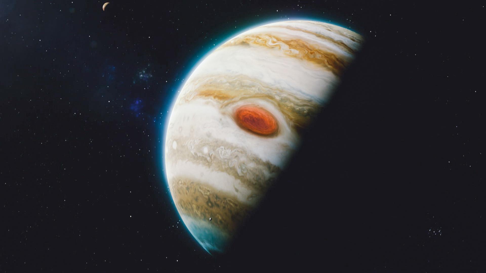  Computeranimation. Ein Planet ist im Halbschatten zur Hälfte zu sehen. Er ist weiß-bräunlich gestreift und hat einen großen roten Fleck. Im Hintergrund ist ein Mond zu sehen.