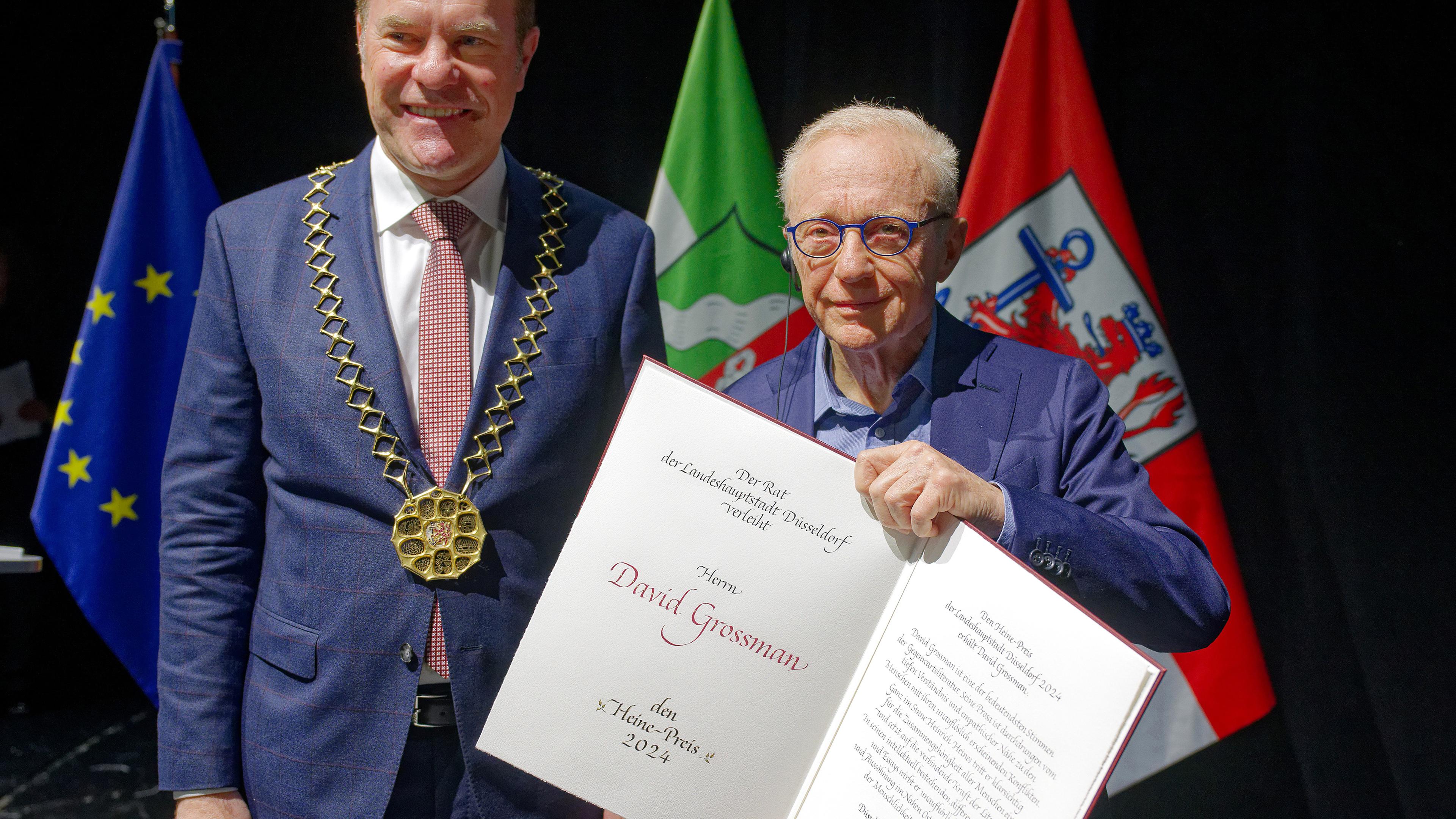 Der Oberbürgermeister von Düsseldorf, Stephan Keller (CDU), und der Autor David Grossman stehen bei der Verleihung des Heine-Preises 2024 an Grossmann auf der Bühne, aufgenommen am 14.12.2024