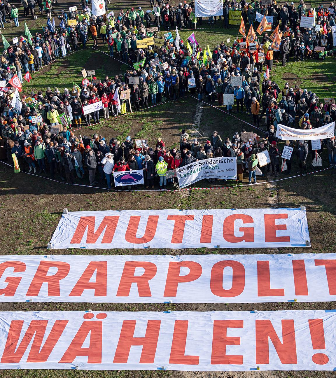 Menschen bilden ein Wahlkreuz während einer Demonstration für eine Agrarwende unter dem Motto «Wir haben es satt!» im Berliner Regierungsviertel auf der Reichstagswiese hinter Bannern mit der Aufschrift "Mutige Agrarpolitik Wählen!"