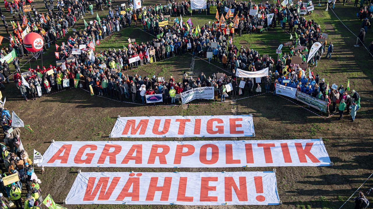 Menschen bilden ein Wahlkreuz während einer Demonstration für eine Agrarwende unter dem Motto «Wir haben es satt!» im Berliner Regierungsviertel auf der Reichstagswiese hinter Bannern mit der Aufschrift "Mutige Agrarpolitik Wählen!"