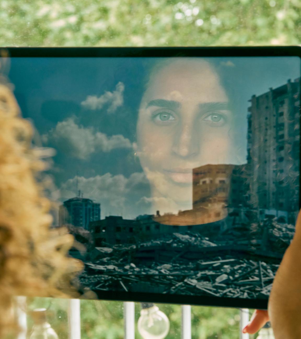 Das Gesicht von Darin Shammout (24) spiegelt sich in einem iPad. Auf dem ihr iPad ist ein Foto einer Trümmerlandschaft in der zerstörte Hochhäuser stehen.