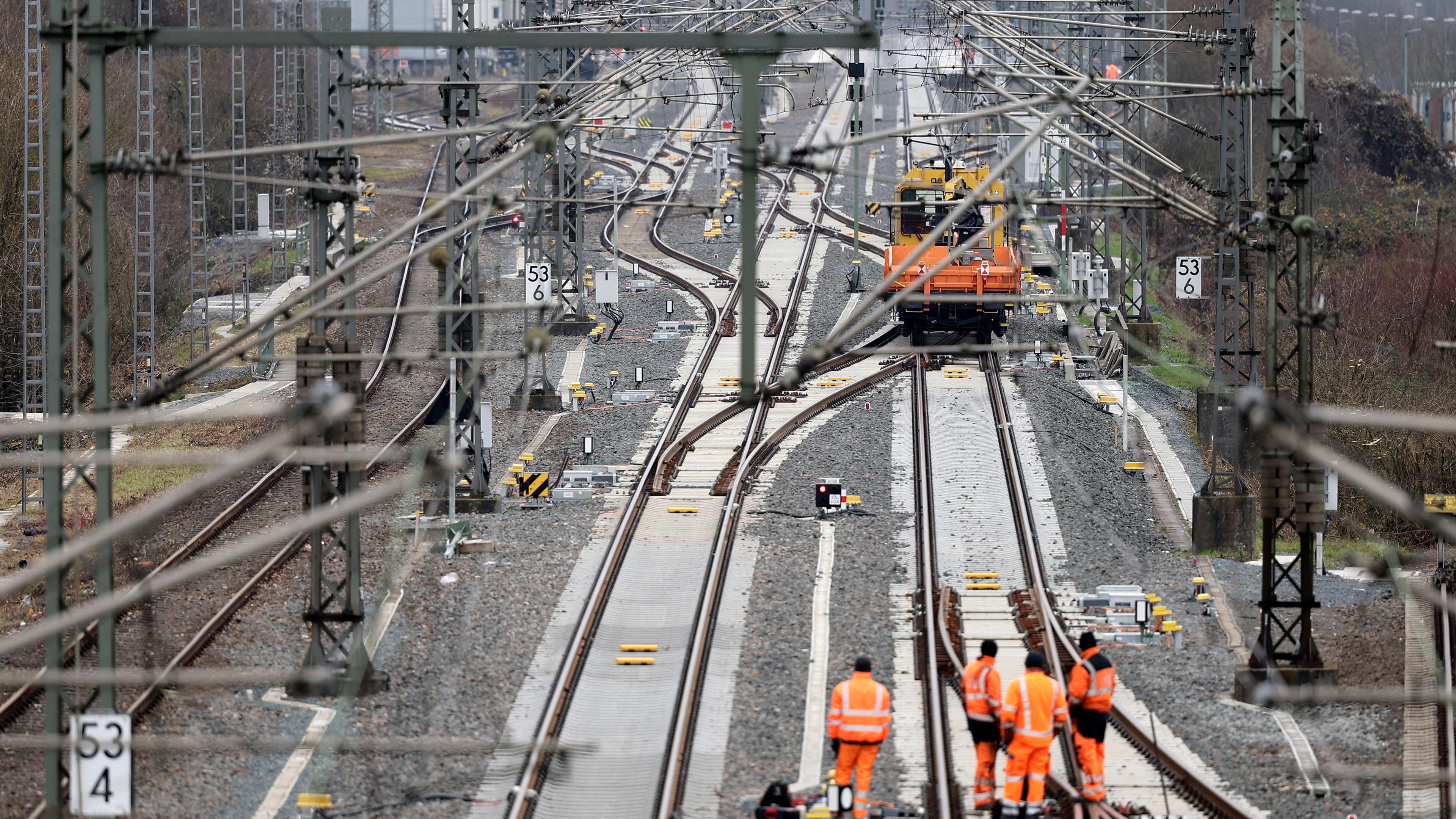 Von oben sind Schienen zu sehen, an denen Arbeiter in orangenen Overalls arbeiten.