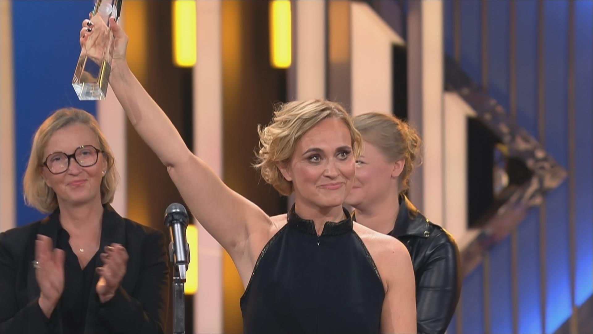 Auf dem Bild ist eine Frau zu sehen, die den deutschen Fernsehpreis in die Höhe hält.