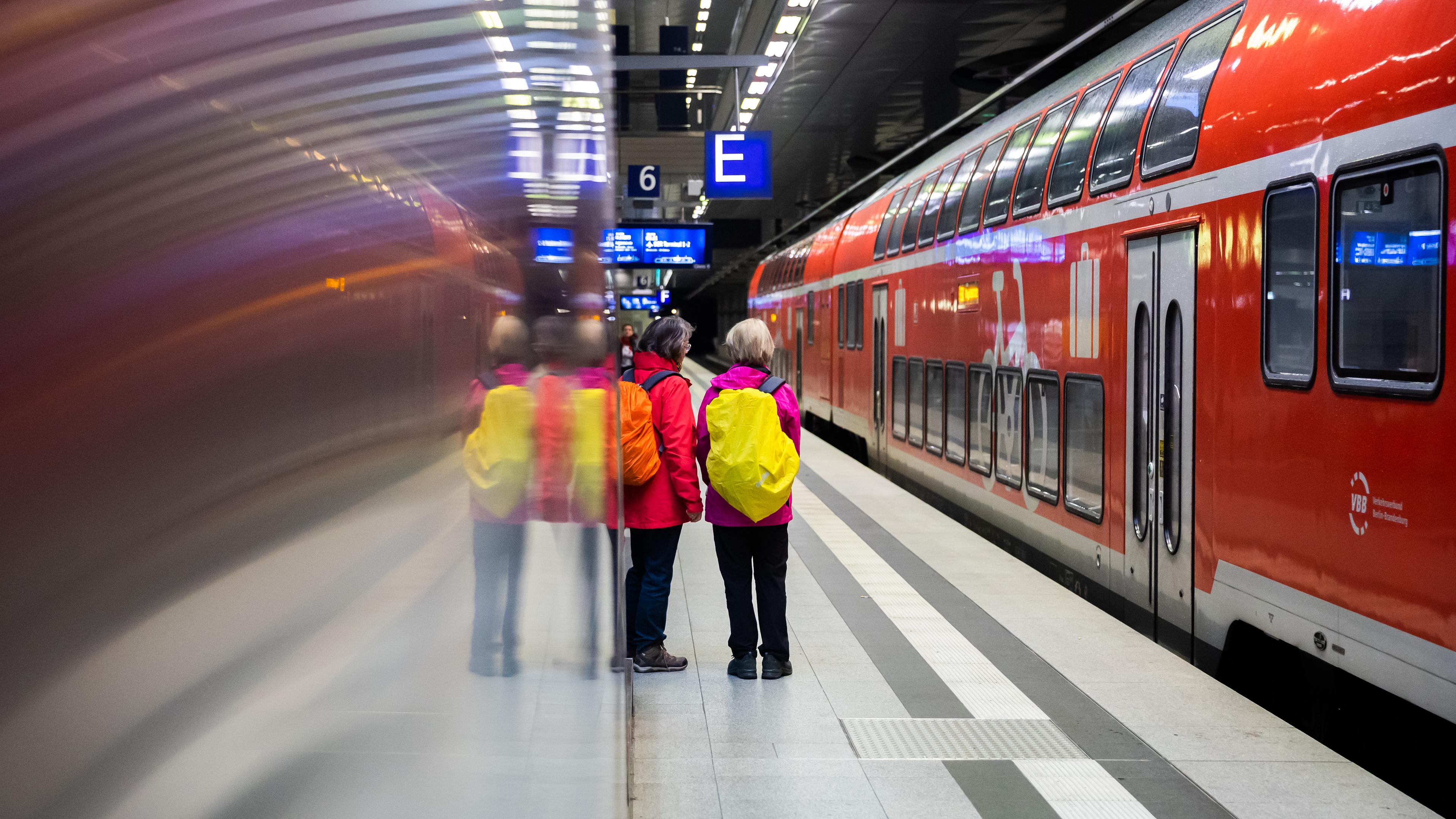 Fahrgäste stehen am Berliner Hauptbahnhof neben einem Regionalexpress am Bahnsteig.