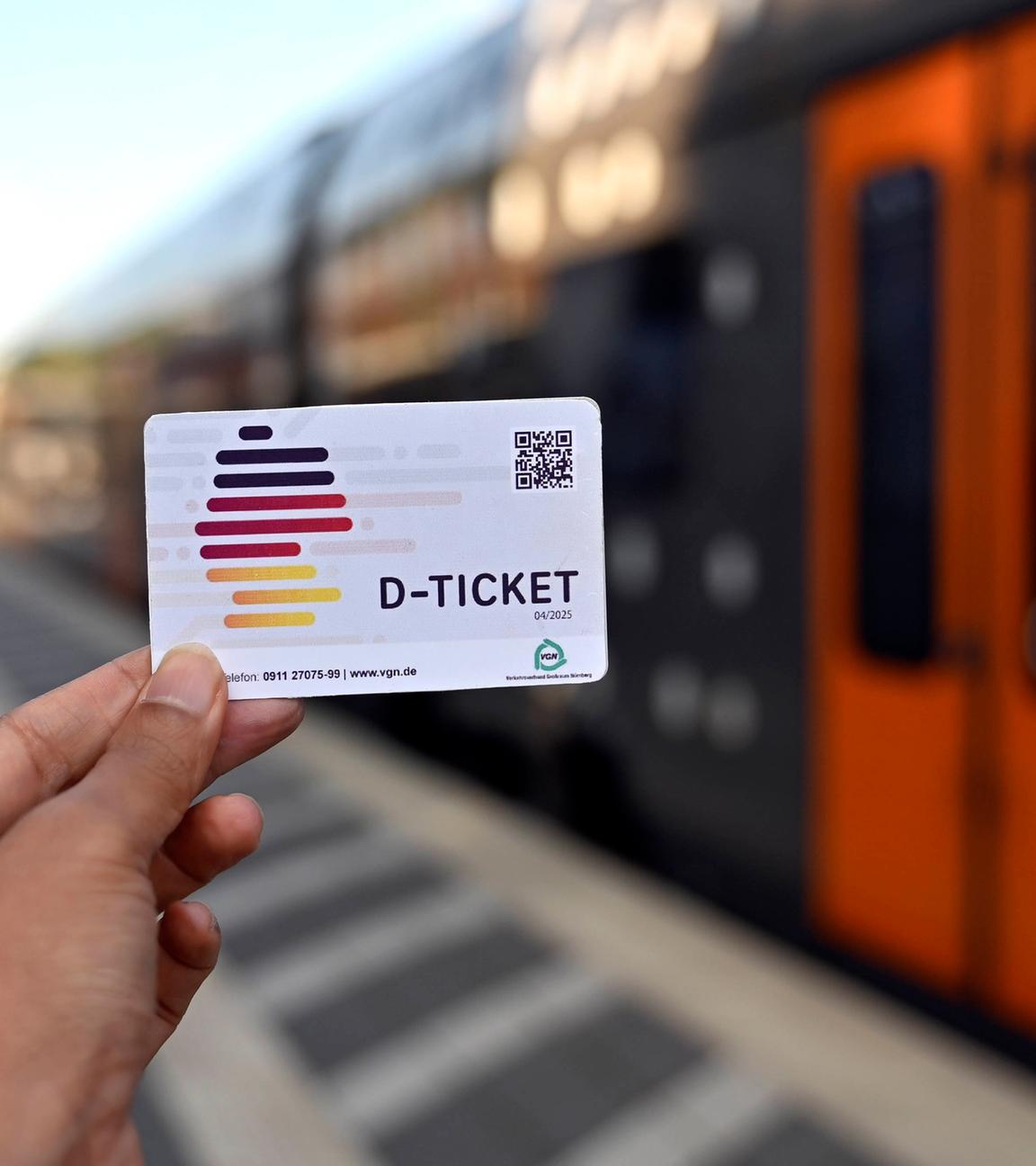 Eine Person hat das Deutschlandticket an einem Bahngleis in der Hand