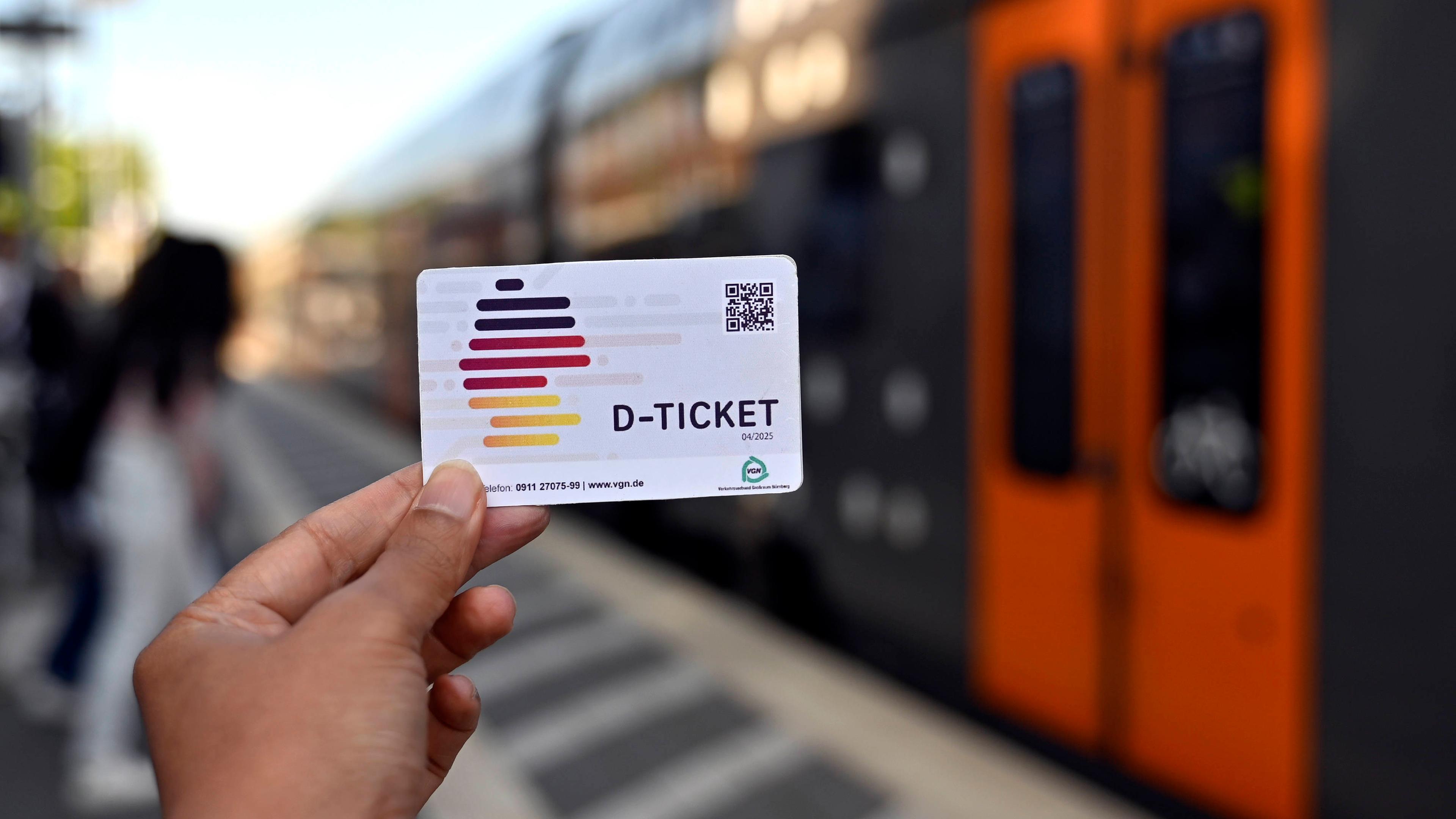 Eine Person hat das Deutschlandticket an einem Bahngleis in der Hand