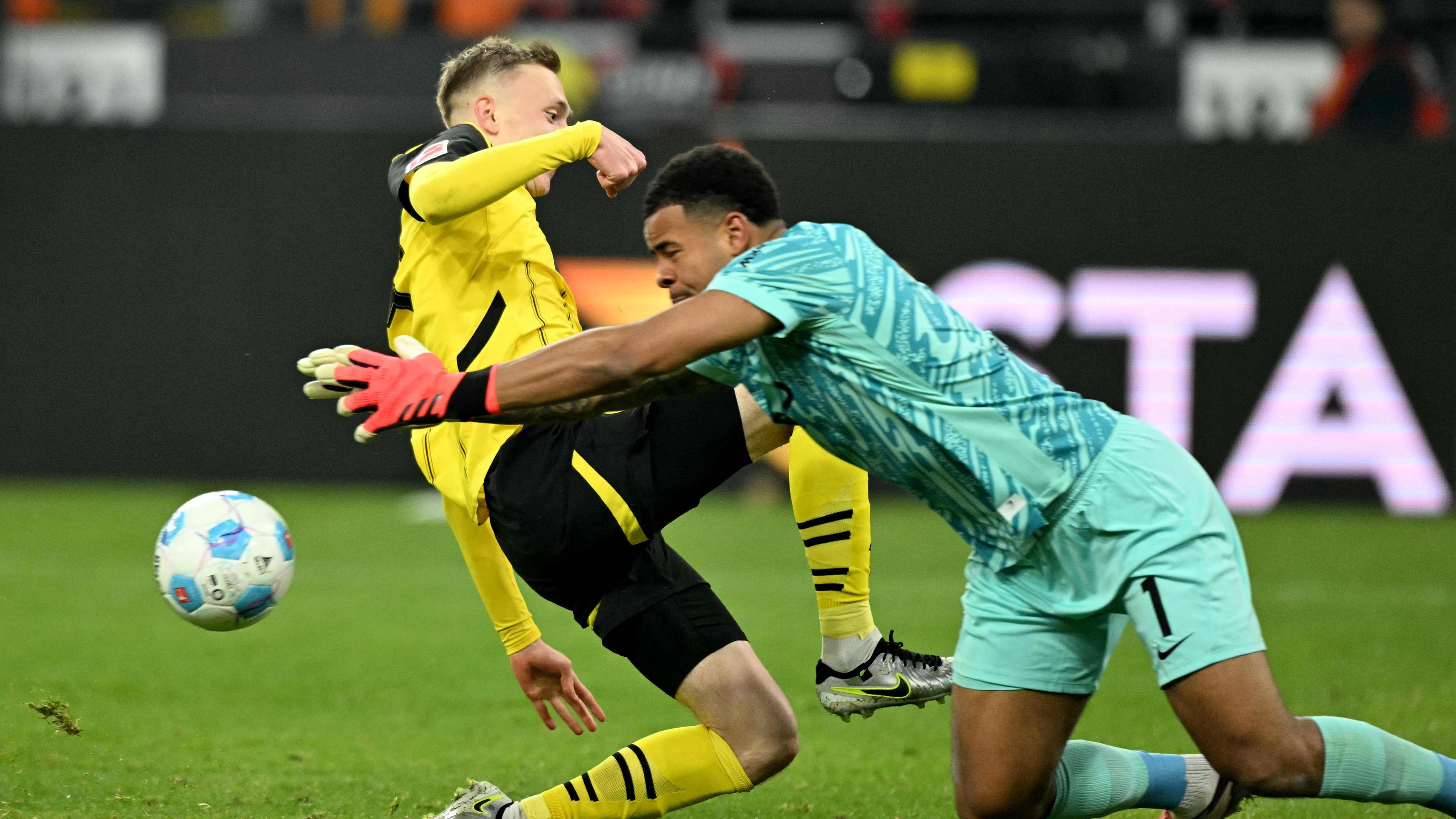 Dortmunds Stürmer (Nr. 14) Maximilian Beier (L) und Freiburgs Torhüter (Nr. 01) Noah Atubolu kämpfen um den Ball.