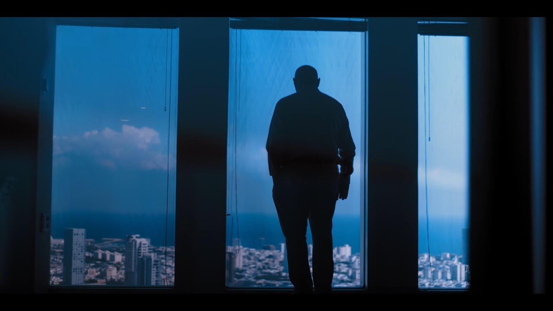 Udi Levi steht mit dem Rücken zur Kamera vor einem großen Fenster und blickt auf Tel Aviv hinab.