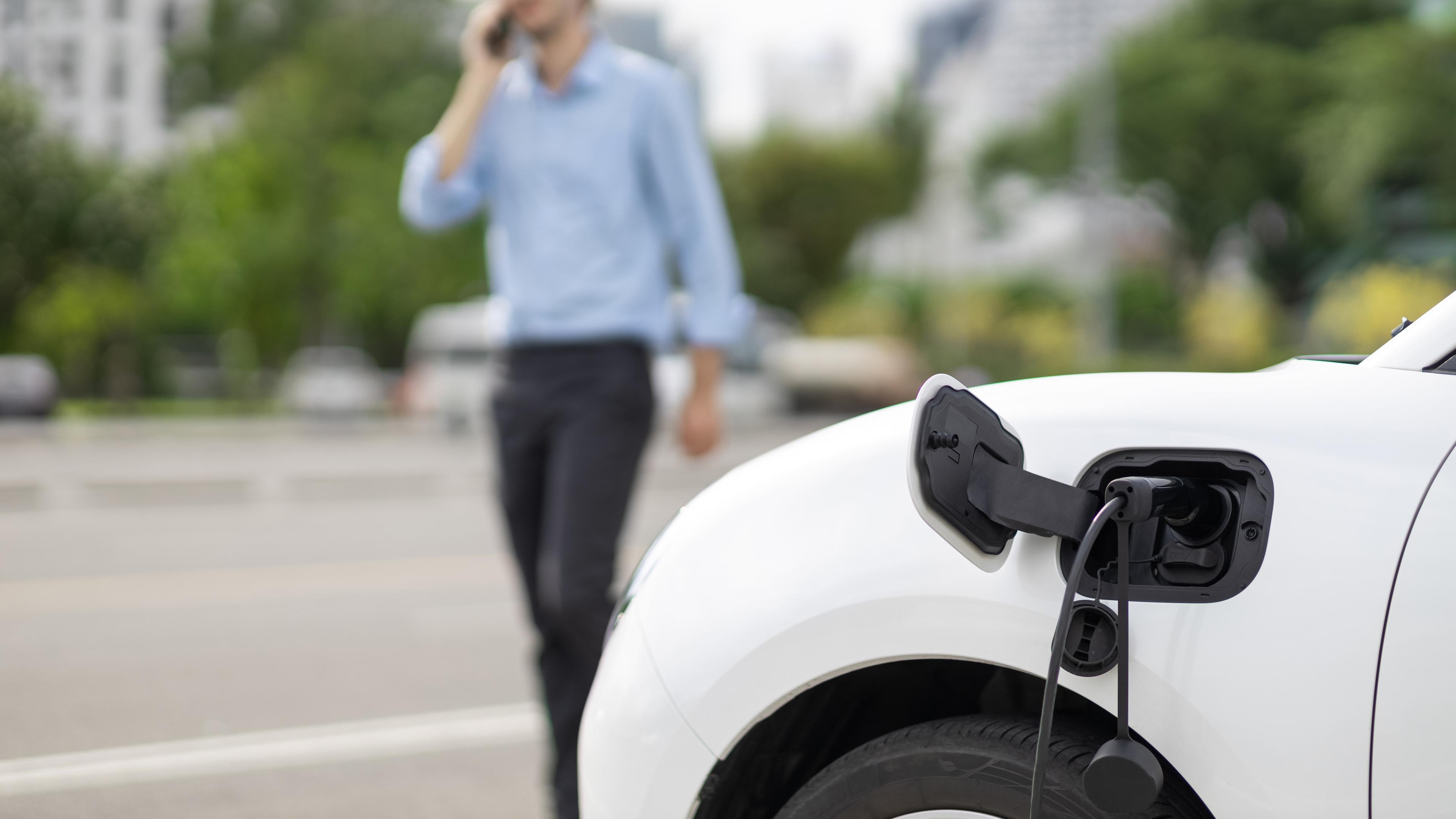 Ein E-Auto lädt während ein Mann daneben telefoniert.