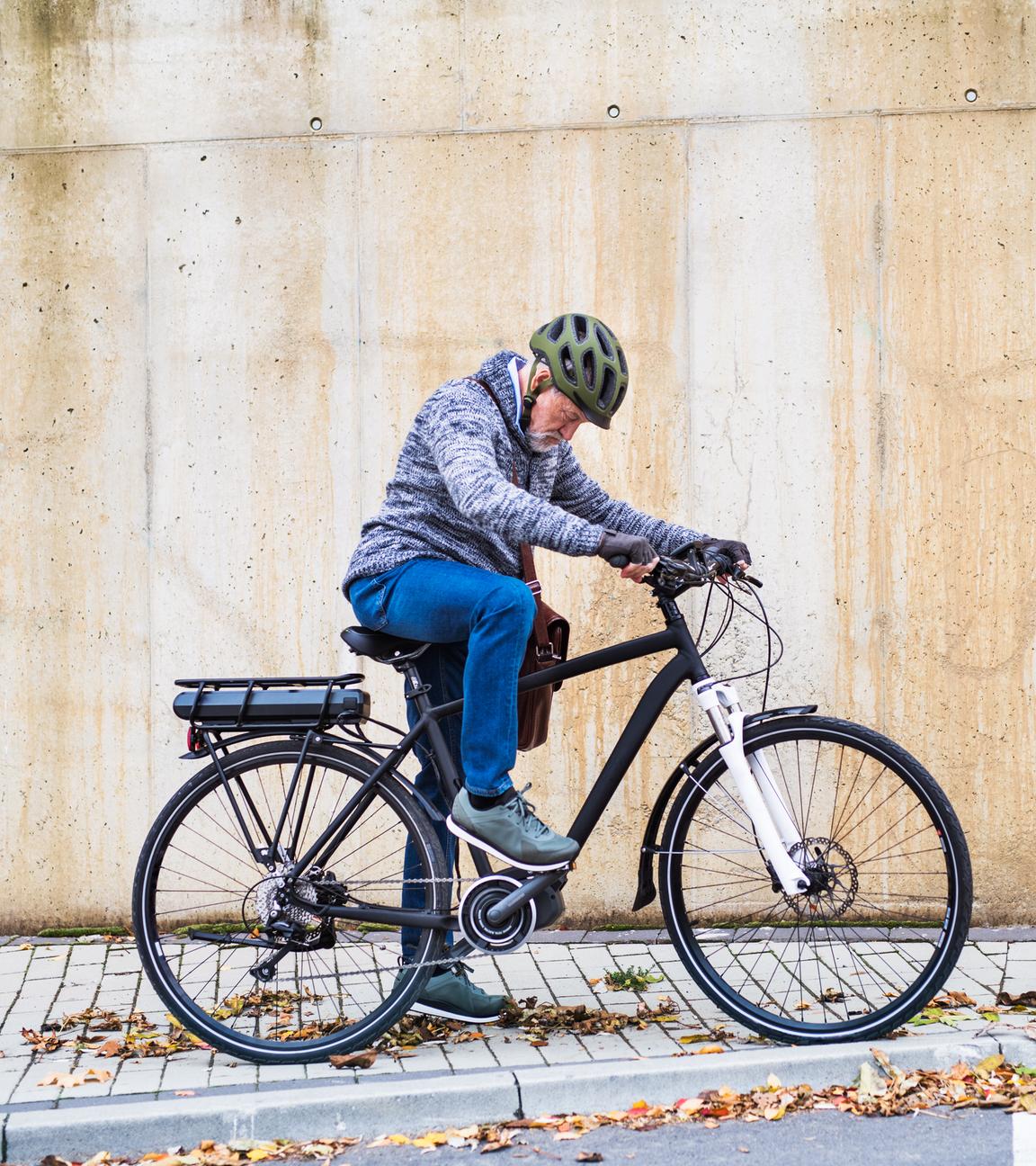 Senior mit Helm steigt auf E-Bike am Straßenrand.