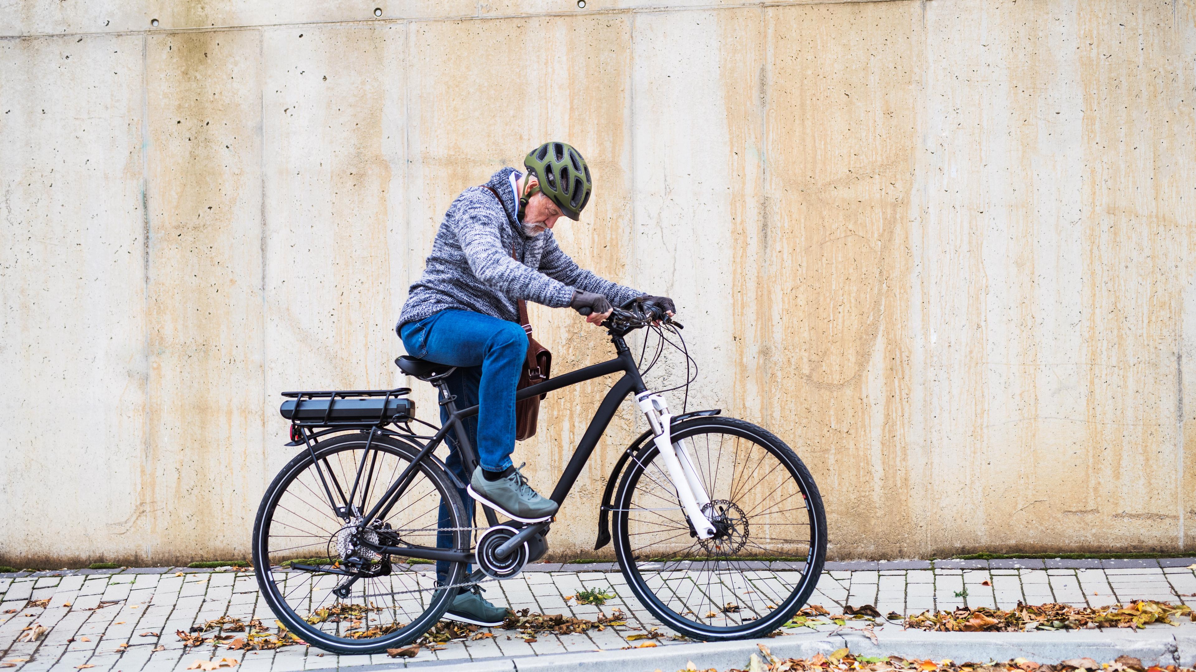 Senior mit Helm steigt auf E-Bike am Straßenrand.