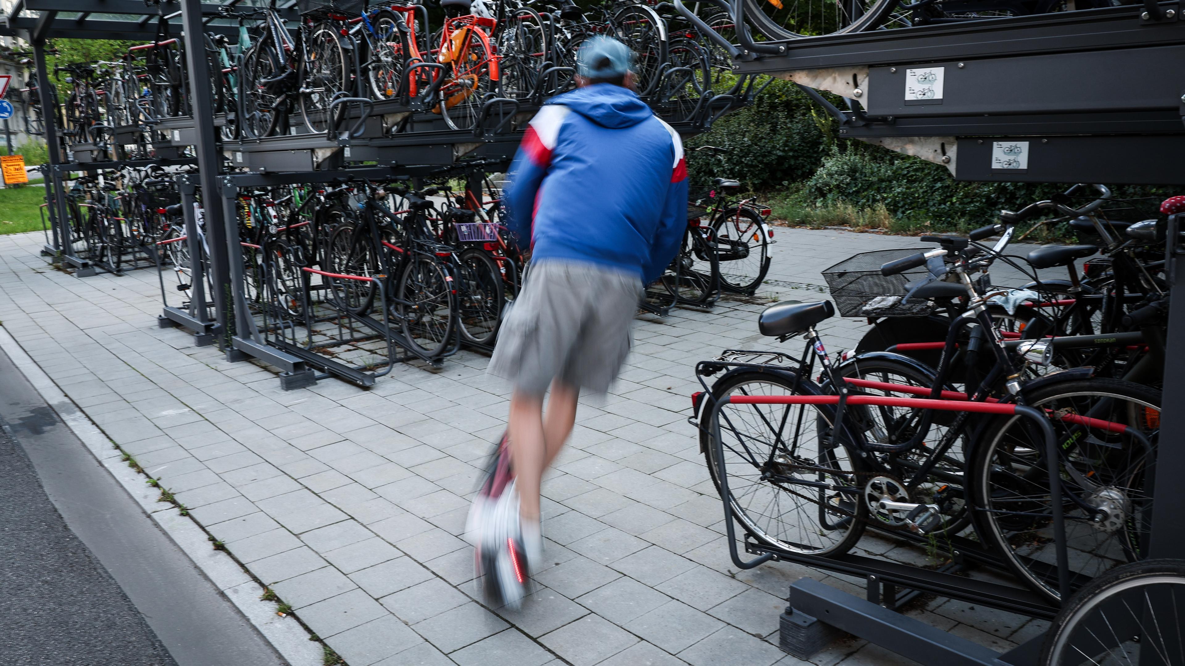  Ein Mann ist mit einem E-Scooter zwischen Fahrradständern an einer U-Bahn-Station unterwegs