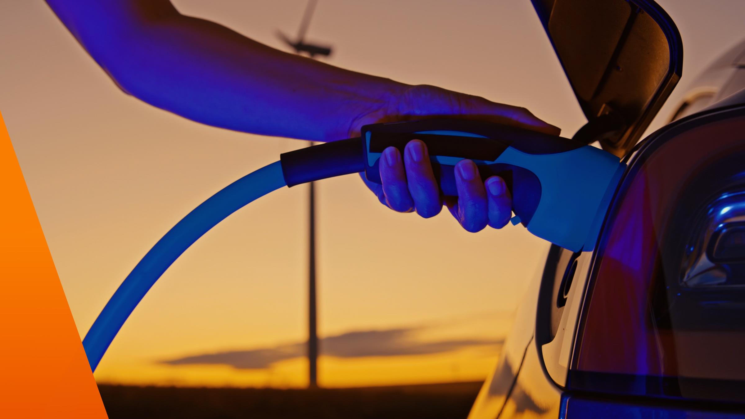 Hand betankt ein Elektroauto mit Strom im Sonnenuntergang