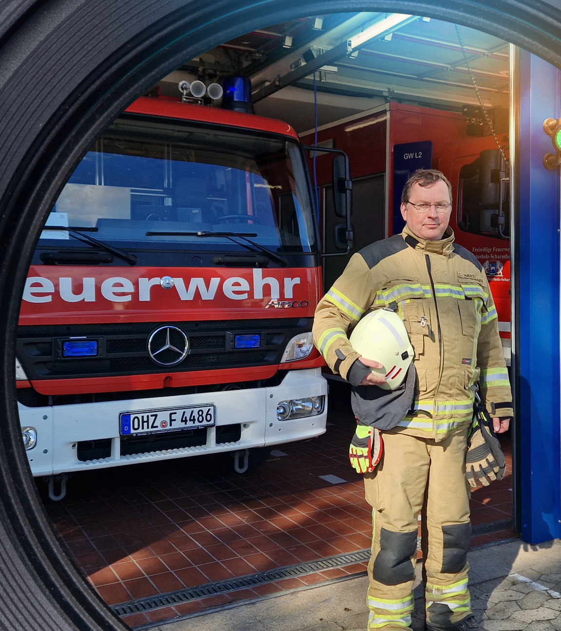 Chris Hartmann steht vor einer Garage mit Einsatzfahrzeugen der Feuerwehr. Er schaut in die Kamera.