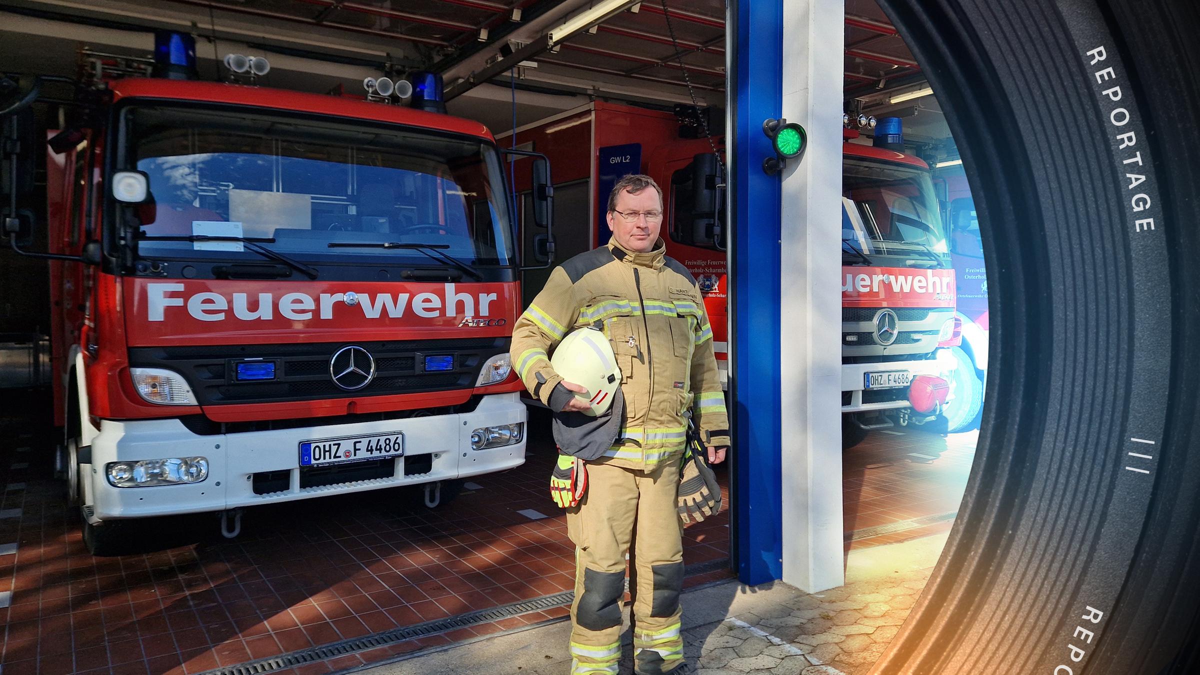 Chris Hartmann steht vor einer Garage mit Einsatzfahrzeugen der Feuerwehr. Er schaut in die Kamera.