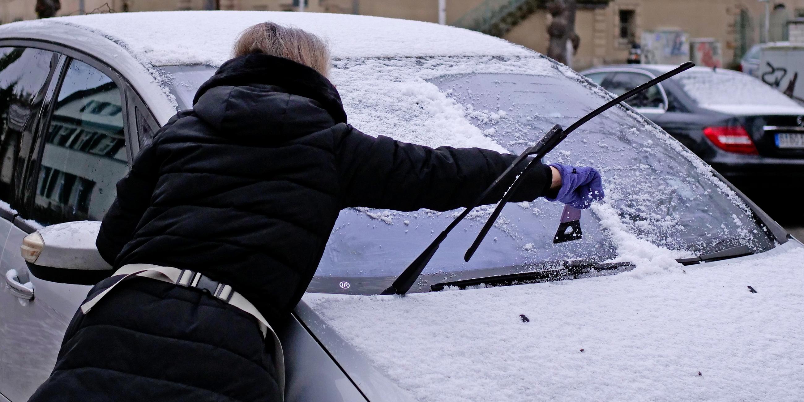 Eine Frau entfernt mit einem Eiskratzer Schnee und Eis von der Frontscheibe ihres Autos.