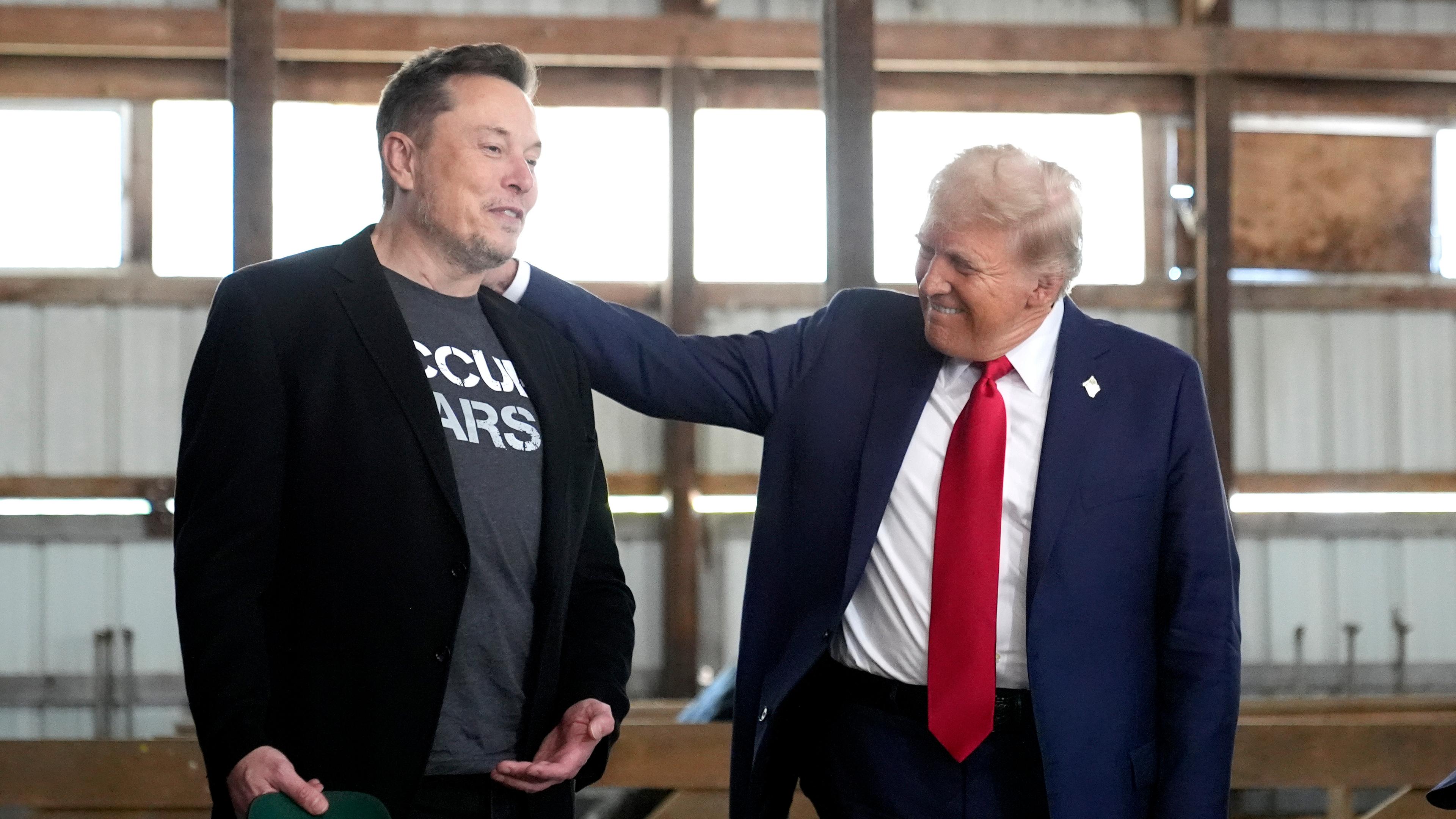 Donald Trump legt Elon Musk die Hand auf die Schulter.