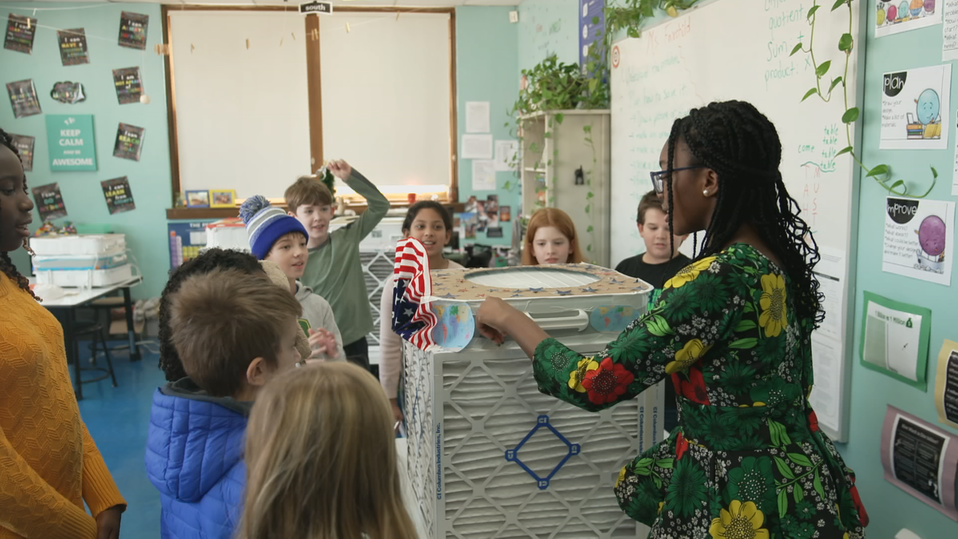 Eniola Shokunbi zeigt Schüler*innen in einem Klassenzimmer den selbstgebauten Luftfilter.